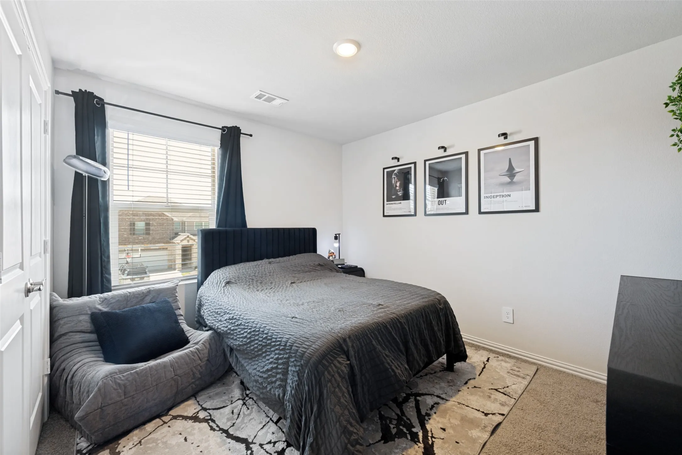 Bedroom featuring a large window with blinds and dark curtains, a gray textured area rug, and neutral wall tones