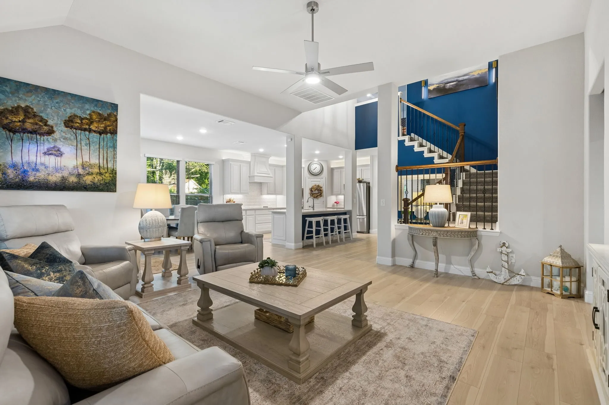 Bright open-concept living area featuring light wood-finish flooring, vaulted ceilings, and a modern ceiling fan
