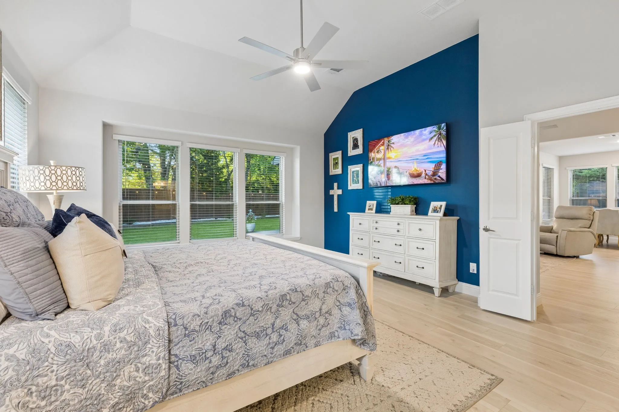 Primary Spacious bedroom featuring vaulted ceilings, light wood-finish flooring, and multiple large windows overlooking a manicured lawn