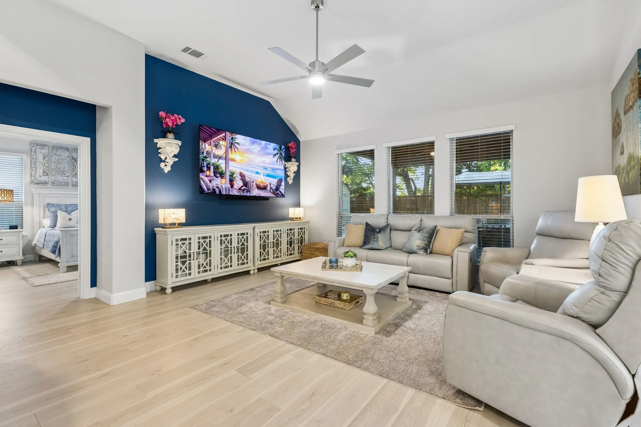 Vaulted ceiling living area featuring light wood-finish flooring, a contemporary ceiling fan, and multiple windows