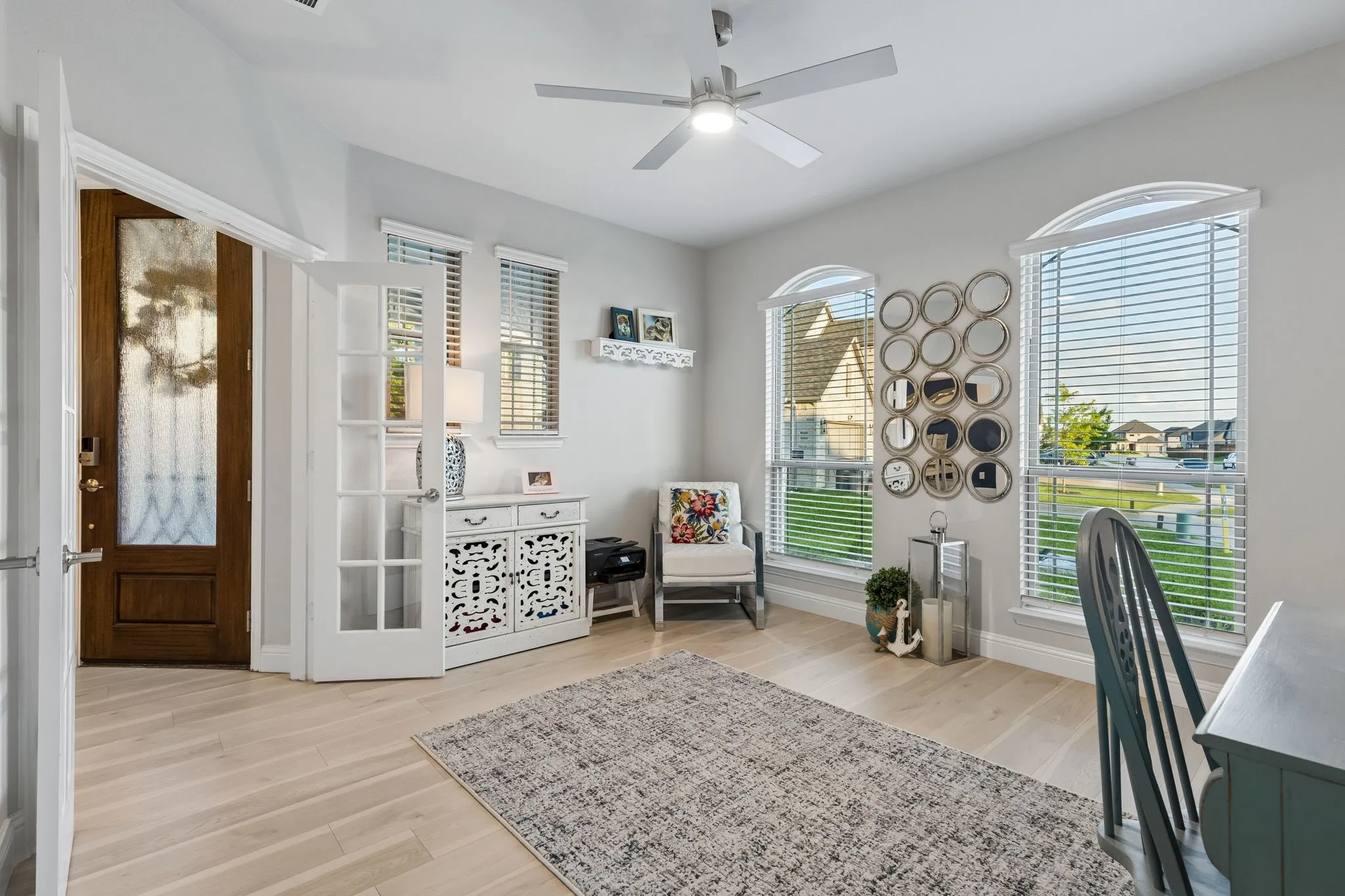 Bright room featuring a wood-finish flooring, a ceiling fan, a decorative white cabinet, and multiple arched windows with blinds