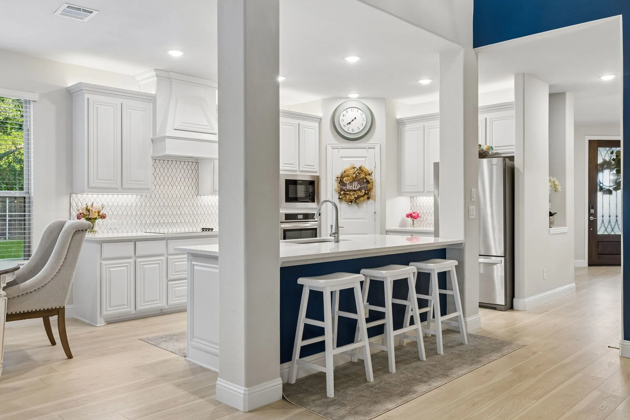 Kitchen featuring white cabinetry, a large central island with a contrasting blue base, light wood-finish flooring, stainless steel appliances, and a custom tiled backsplash