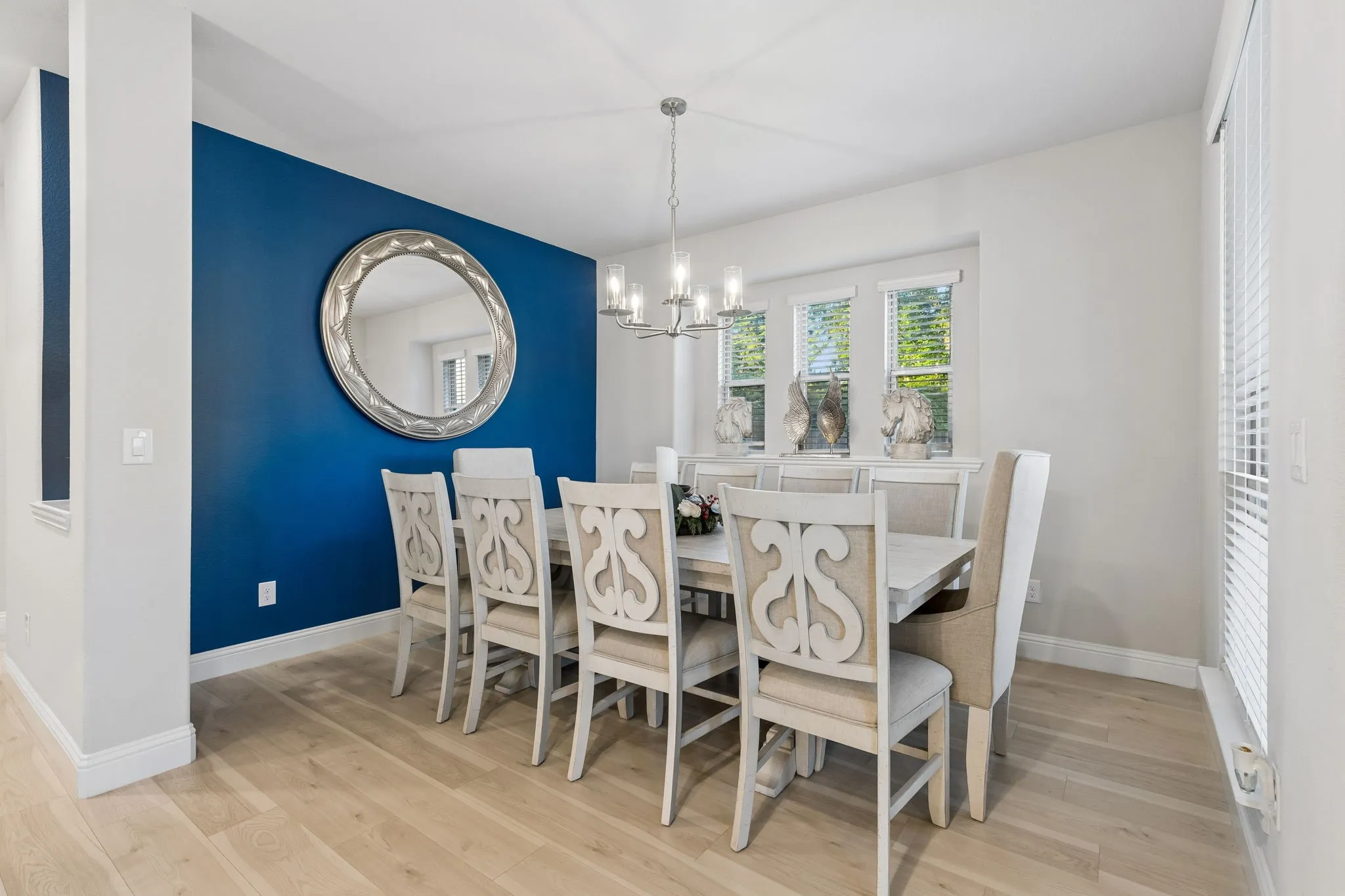 Dining area featuring light wood-finish flooring, a contemporary chandelier, a prominent accent wall, multiple windows, and ample space for entertaining.