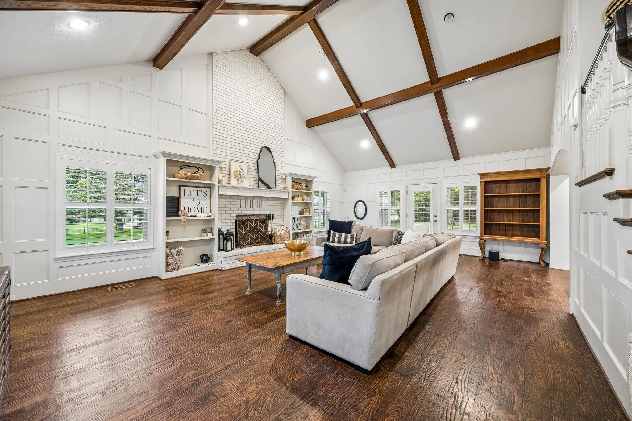 Expansive living room with beamed vaulted ceiling, wood floors, brick fireplace and built-ins.