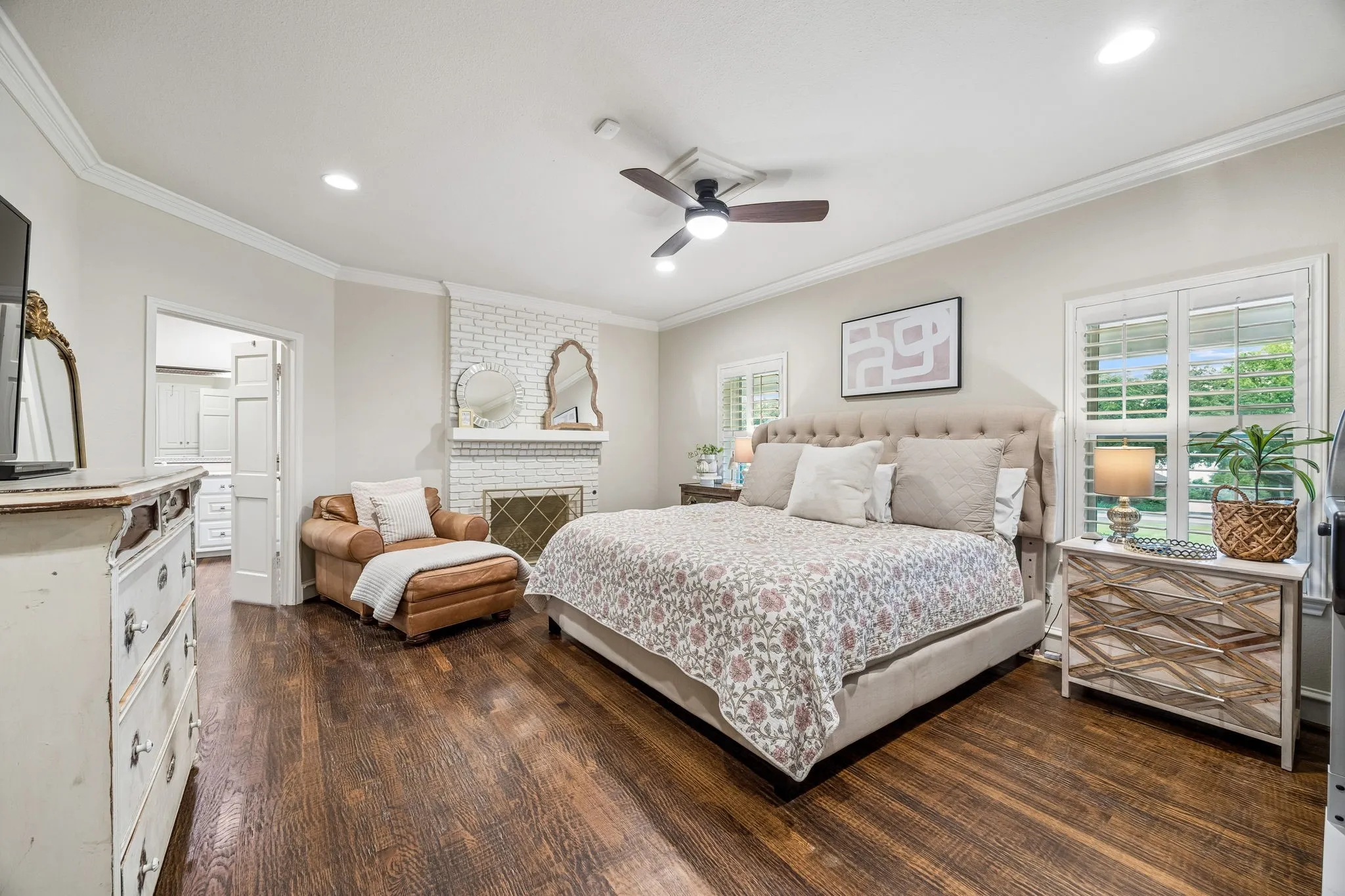 Spacious primary bedroom with wood floor, fireplace and crown molding.  The fireplace is not used.