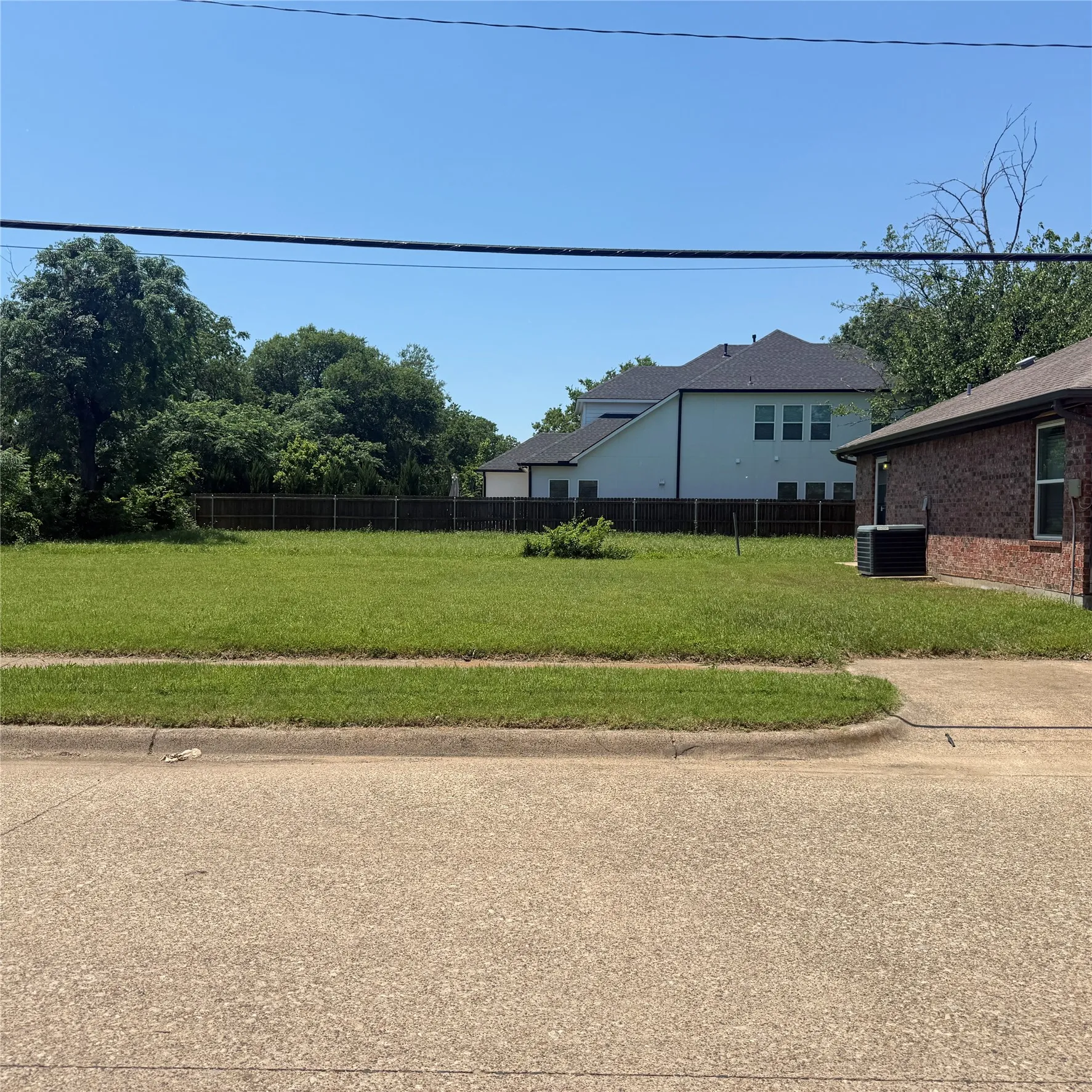 Expansive level lot featuring green grass, a concrete curb, and a partial privacy fence at the rear