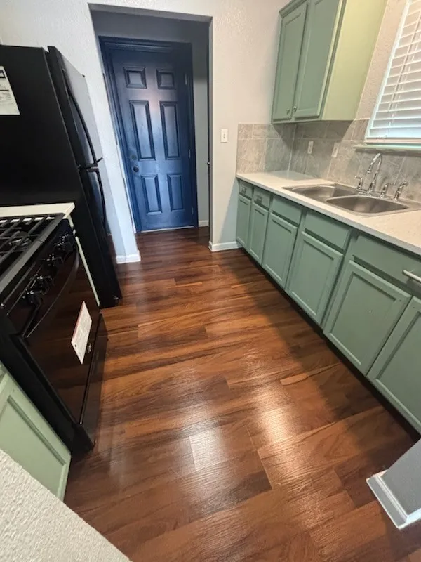 Kitchen featuring wood-finish flooring, two-tone cabinetry with light green lower and upper cabinets, a dual basin stainless steel sink, and a black appliance suite