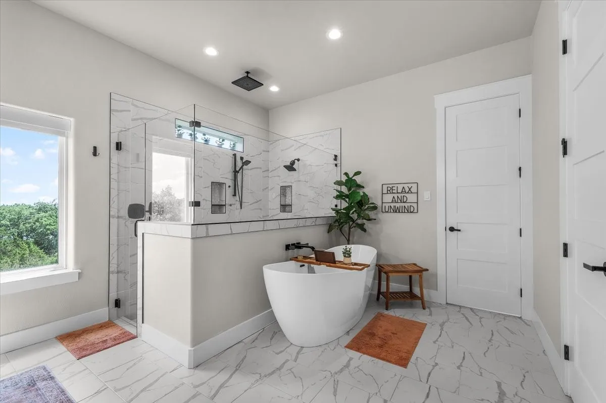 Primary bathroom featuring a freestanding soaking tub, a spacious glass-enclosed shower with multiple showerheads, and large format marble-look tile flooring