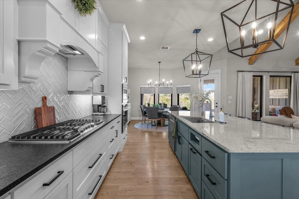 Gourmet kitchen with a gas range, herringbone tile backsplash, custom range hood and expansive center island with an undermount sink