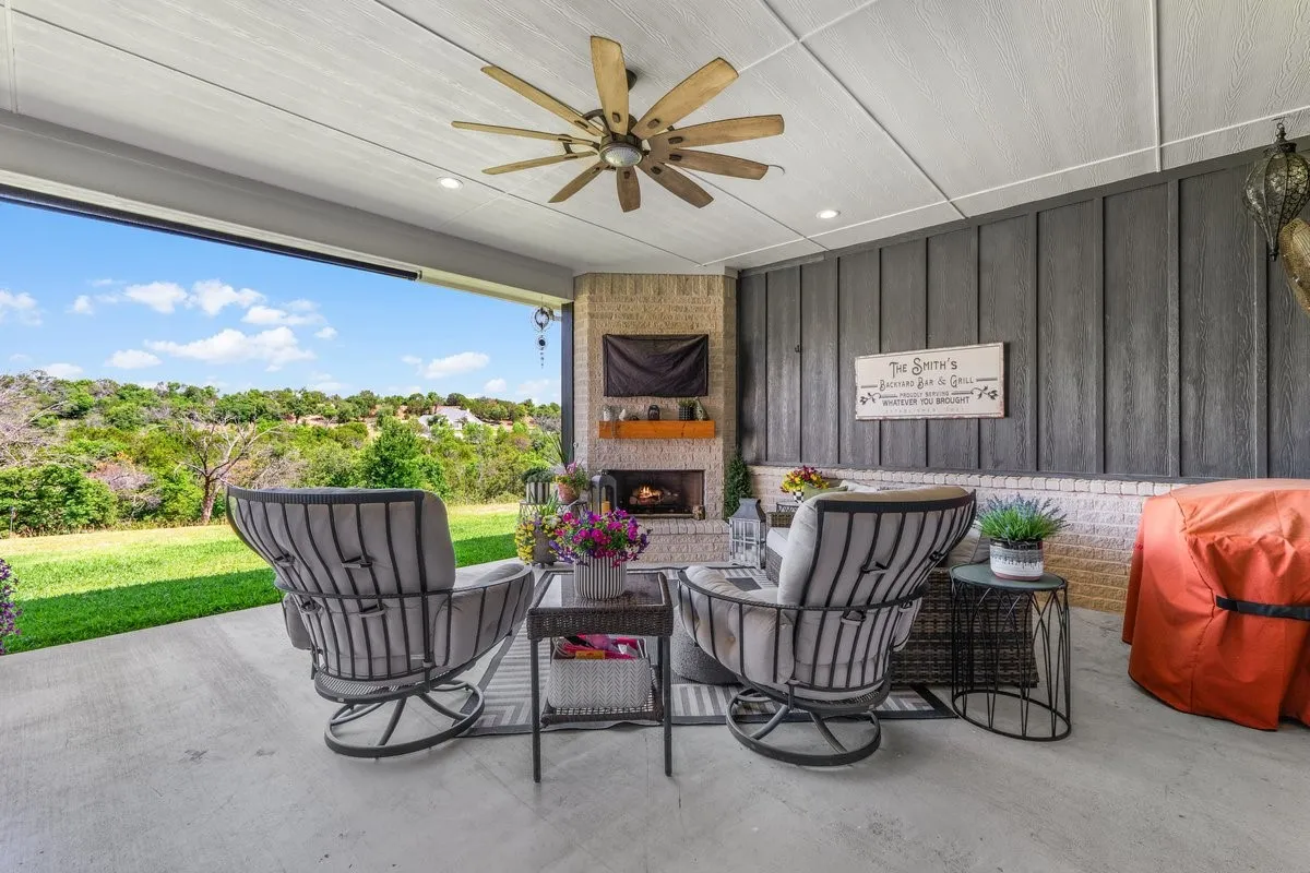 Covered outdoor patio featuring a ceiling fan, recessed lighting, and a stone-clad fireplace with a wood mantel