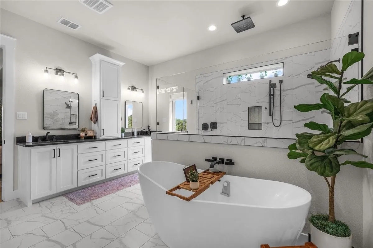 Primary bathroom featuring a freestanding soaking tub, a spacious glass-enclosed shower with multiple showerheads, and large format marble-look tile flooring