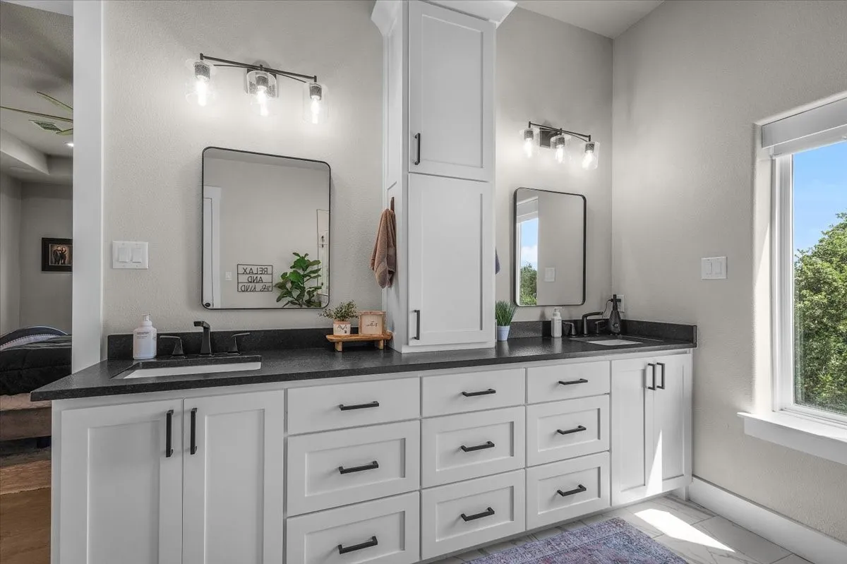 Dual vanity with white cabinetry, black hardware, granite countertops, hidden plugs in the drawers and cabinets and a natural light