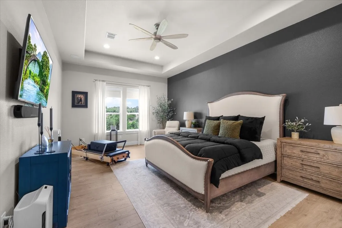 Primary room featuring a tray ceiling with a ceiling fan, recessed lighting, roller shades and accent wall.
