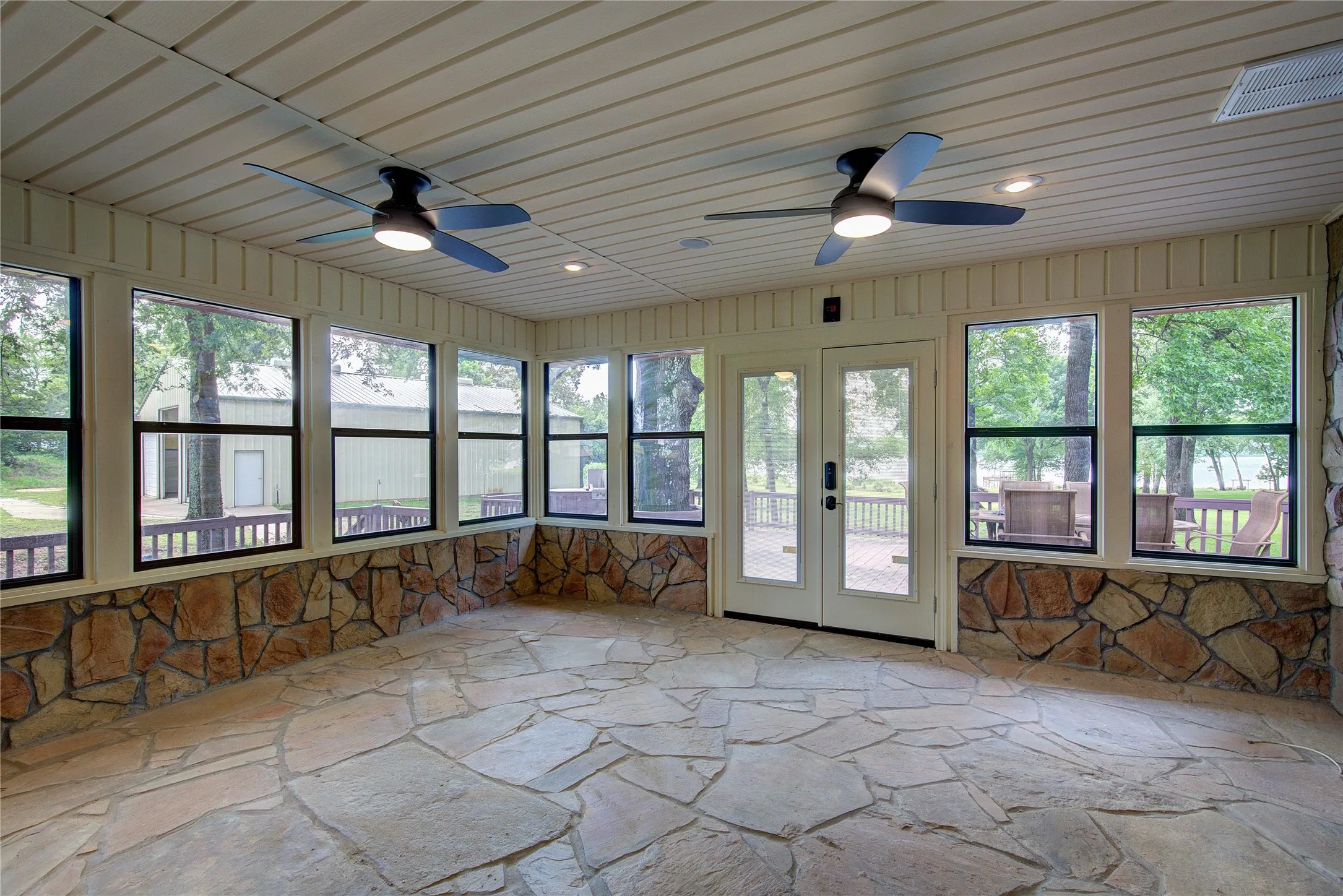 Enclosed sun room has flagstone floor, wooden ceiling, two ceiling fans, french doors to deck