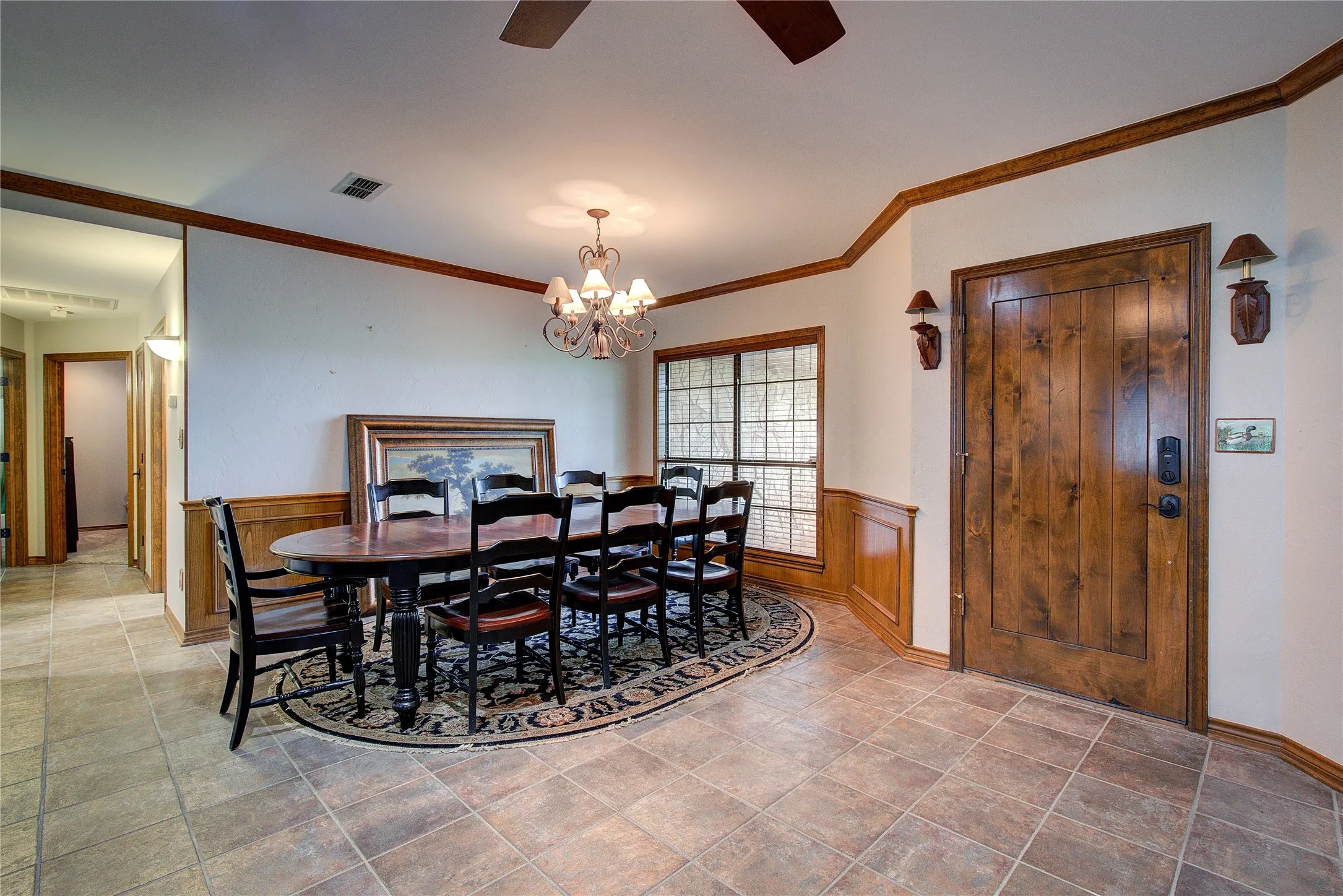 Solid wood entry door leads into a formal dining space with crown molding and wainscoting.