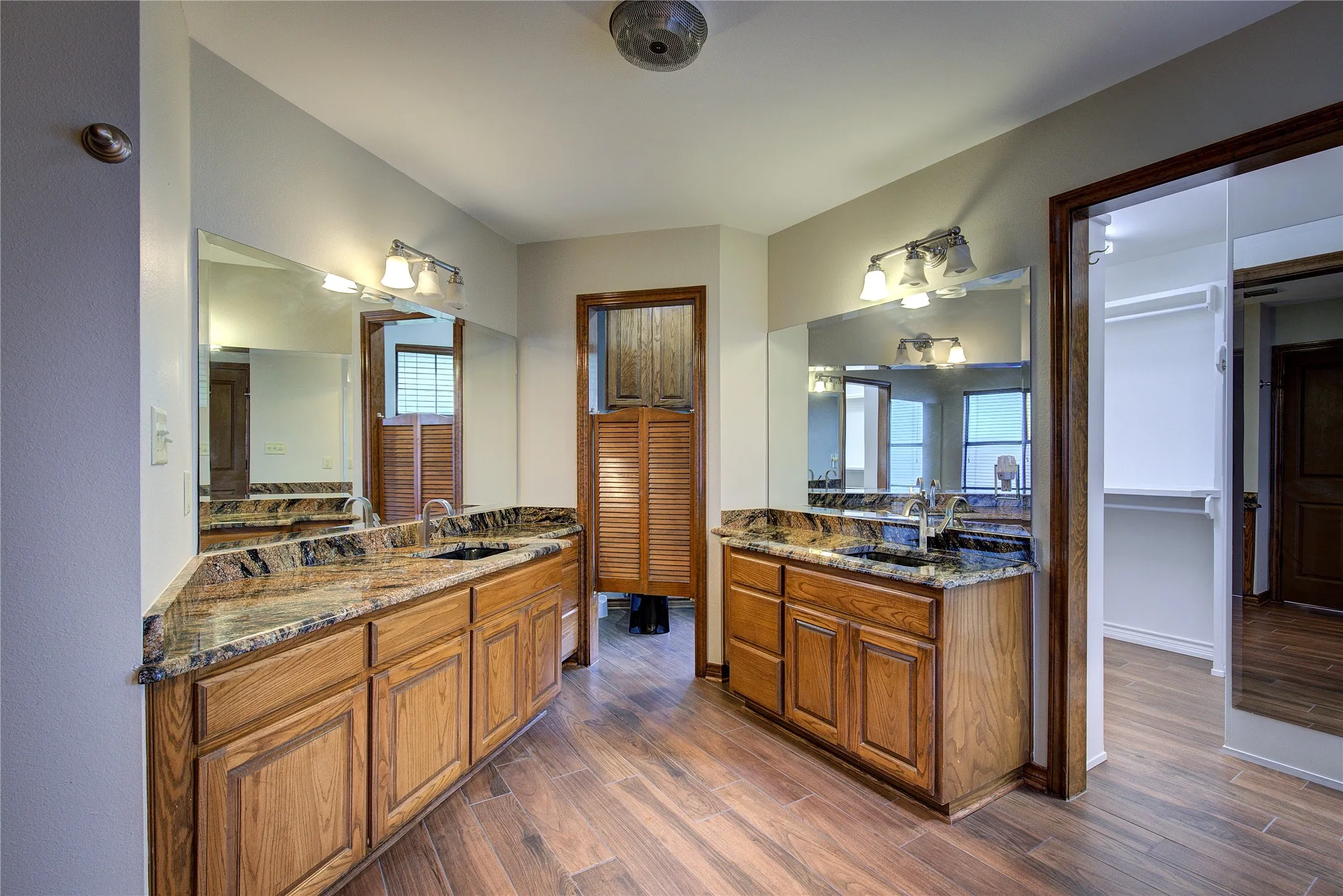 Primary bath has separate vanities with granite counters, custom wood cabinetry, LVP flooring, private potty, huge walk-in closet with custom shelving.