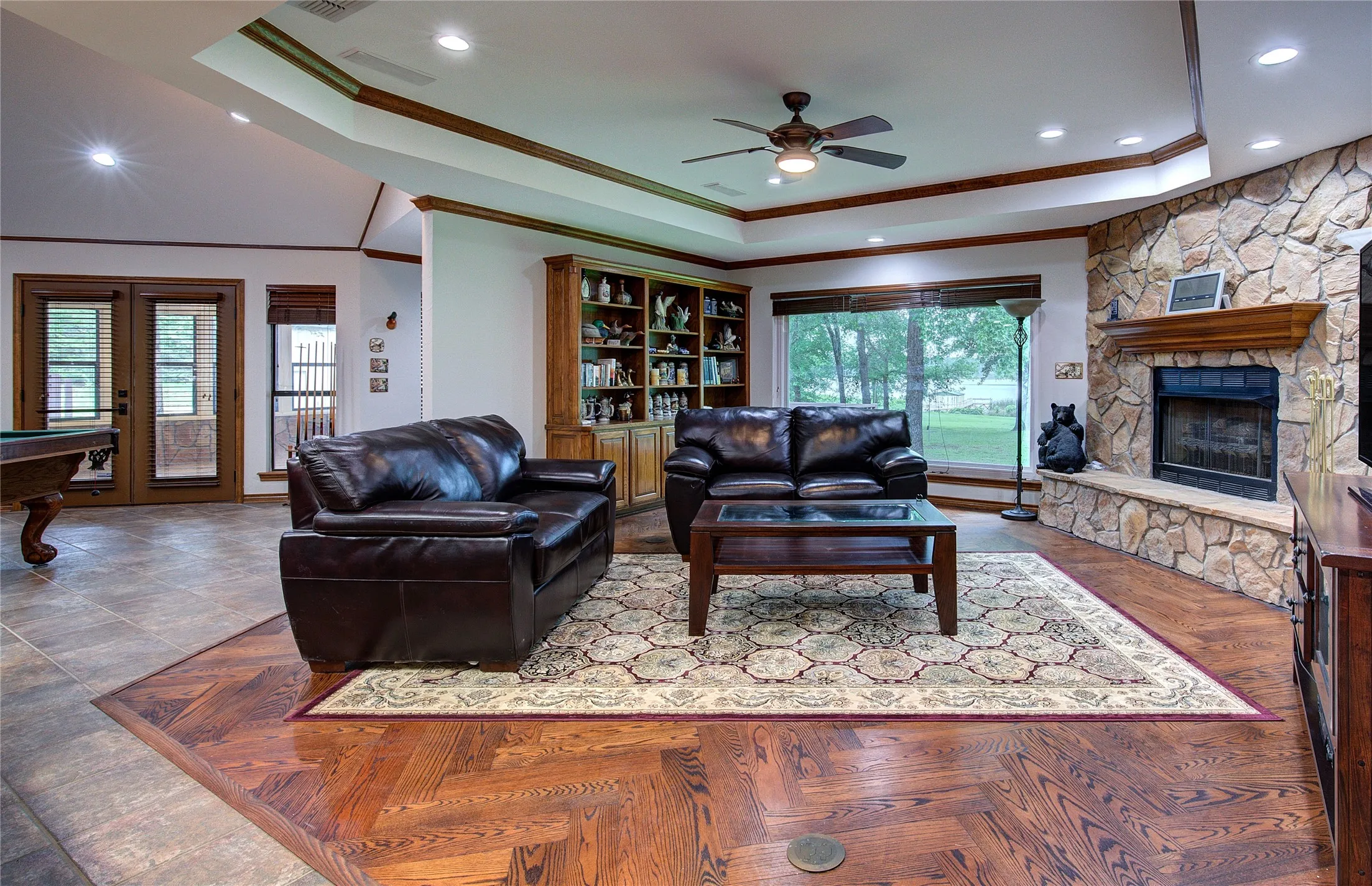 Living room has wood floor, raised ceiling and wall of windows overlooking the lake, plus stone gas fireplace with glass doors.