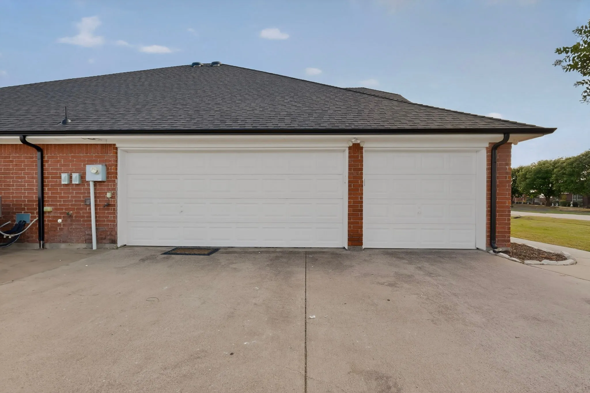 Brick exterior featuring two white garage doors and a dark shingle roof