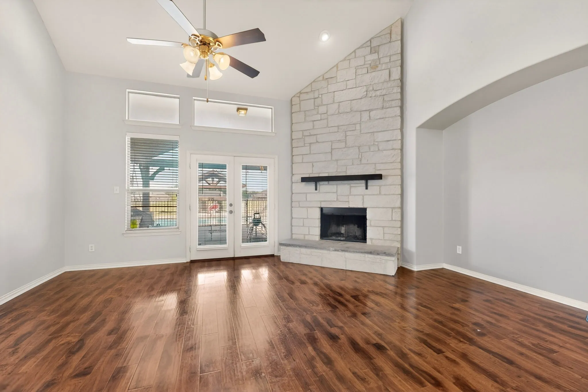 Spacious living area featuring high vaulted ceilings, wood-finish flooring, and a stone fireplace with a raised hearth