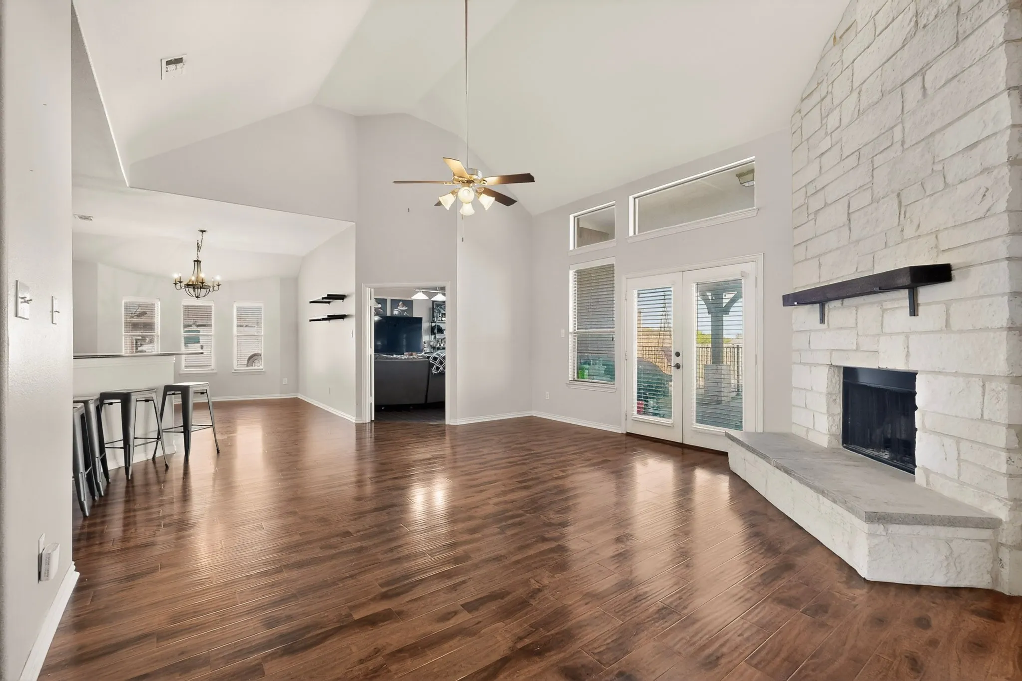 Spacious living area featuring wood-finish flooring, a stone fireplace with a dark wood mantel, and vaulted ceilings