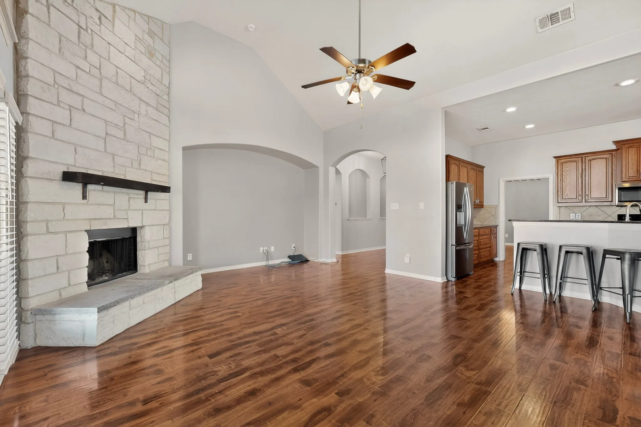 Spacious living area featuring wood-finish flooring, a stone-faced fireplace with a hearth, and a vaulted ceiling