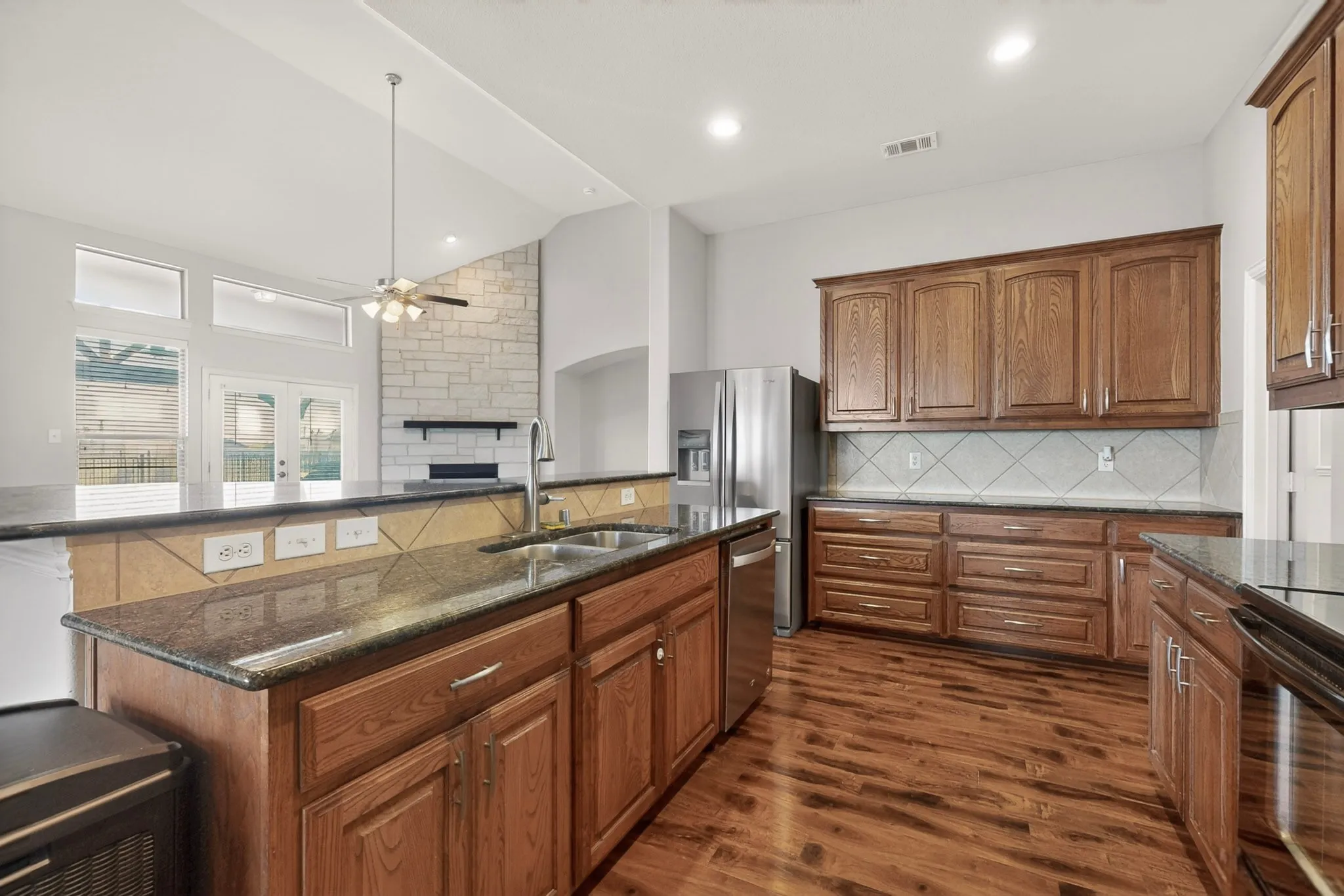 Kitchen featuring wood-finish flooring, granite countertops, wood cabinetry, and a stainless steel refrigerator