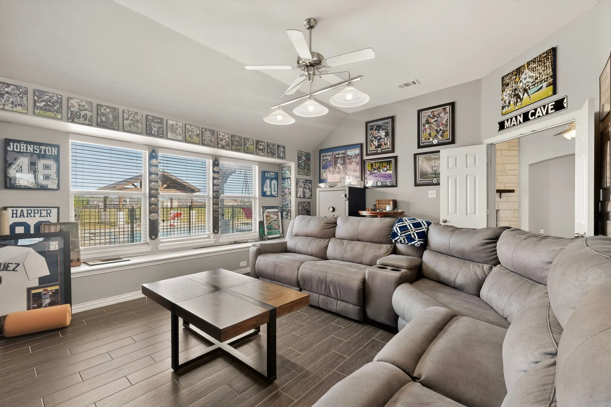Spacious recreational room featuring wood-finish flooring, a contemporary ceiling fan with integrated lighting, and multiple large windows with horizontal blinds
