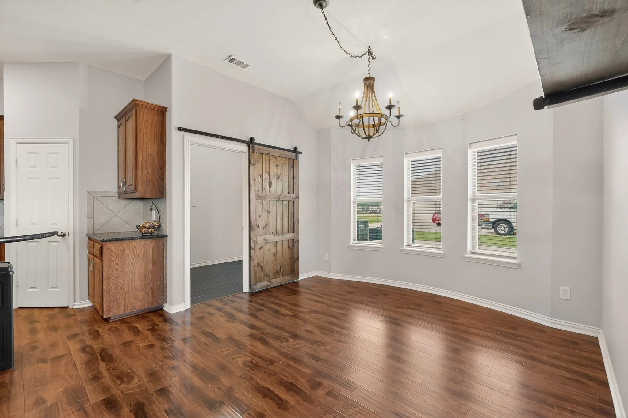 Open-concept dining area featuring wood-finish flooring, a rustic chandelier, and a bay of three windows with blinds
