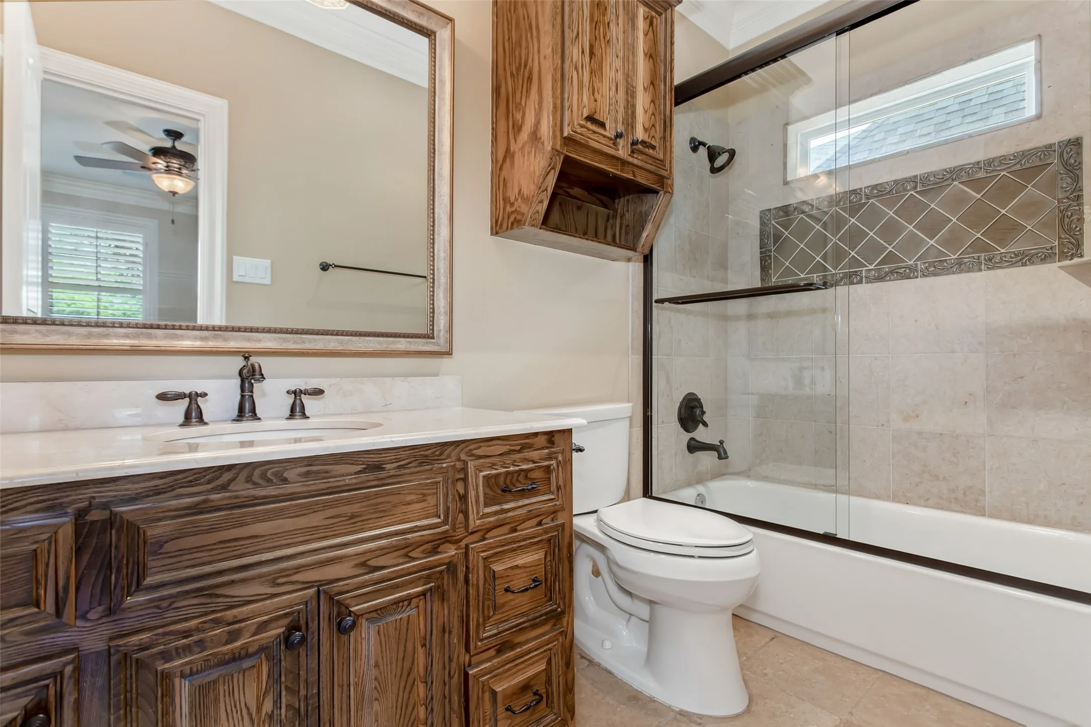 Private ensuite bath featuring custom wood cabinetry, stone countertops, and a tub/shower combination with frameless glass enclosure and designer tile surround.