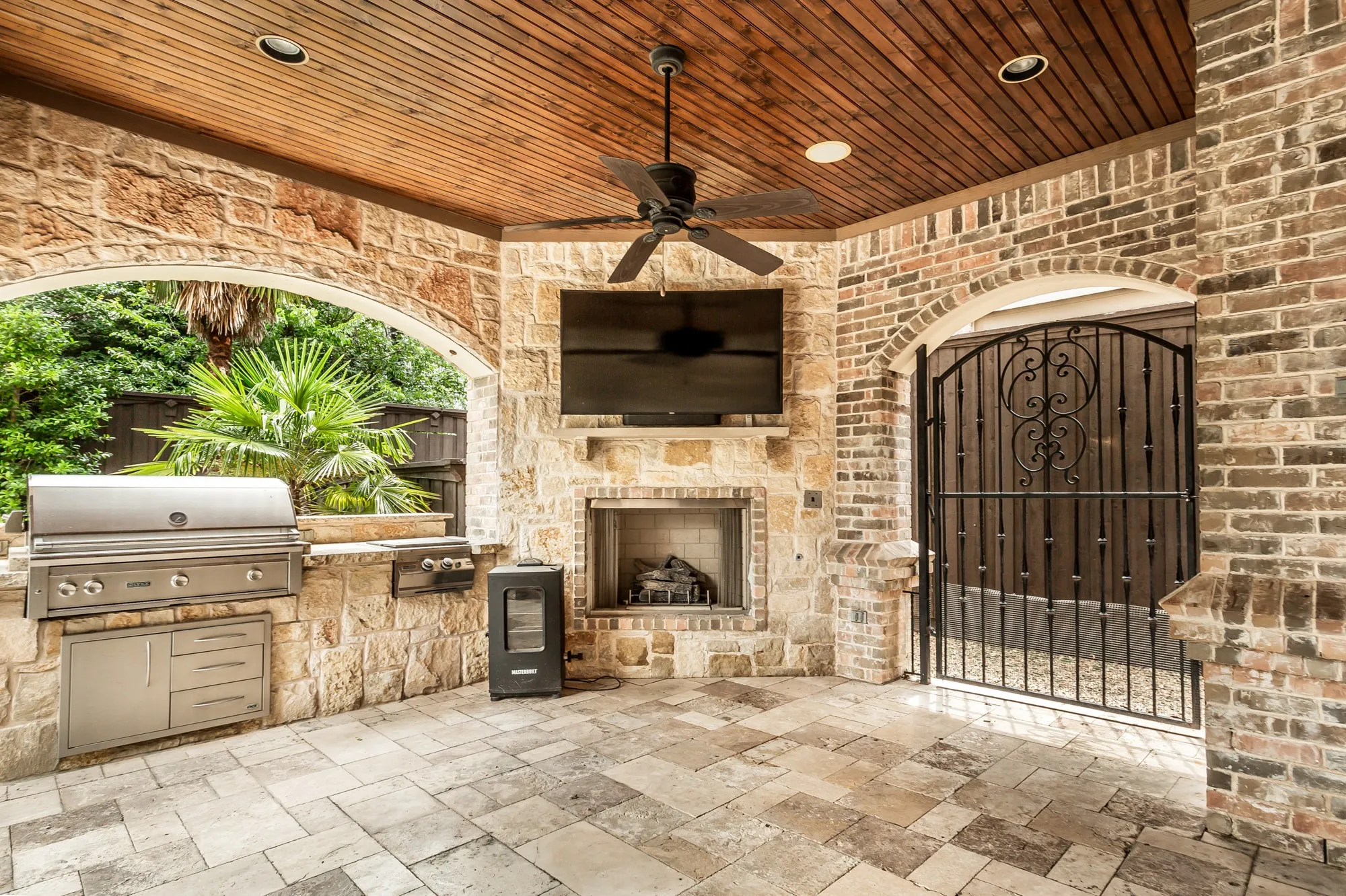 Designed for year-round entertaining, the expansive covered outdoor living area is a true extension of the home. A rich wood-plank ceiling with recessed lighting, ceiling fans, and built-in speakers creates an inviting atmosphere, while the impressive stone fireplace with mounted television serves as the centerpiece for outdoor gatherings.