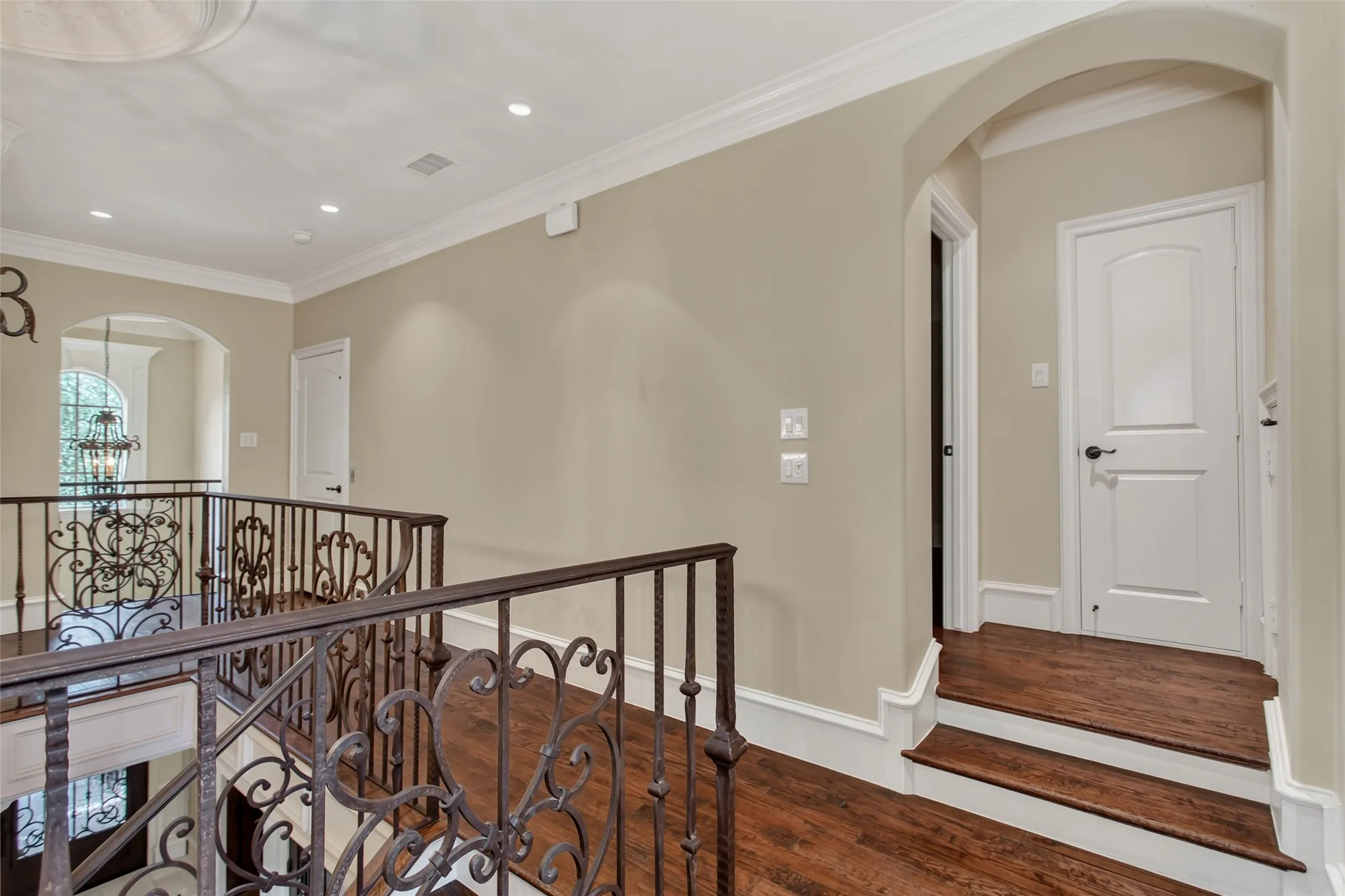 The open upper-level gallery overlooks the dramatic living area below, showcasing decorative wrought-iron railings, hardwood flooring, soaring ceilings, and thoughtfully designed access to the secondary bedrooms.
