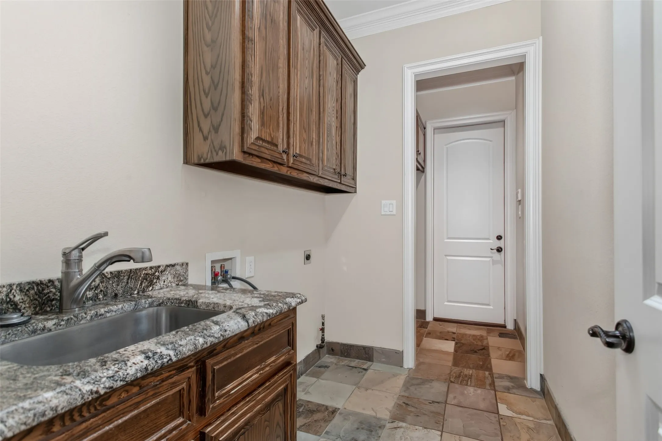 Spacious utility room with full-size washer and dryer connections, utility sink, custom cabinetry, granite countertops, and dedicated space for a second refrigerator or freezer.