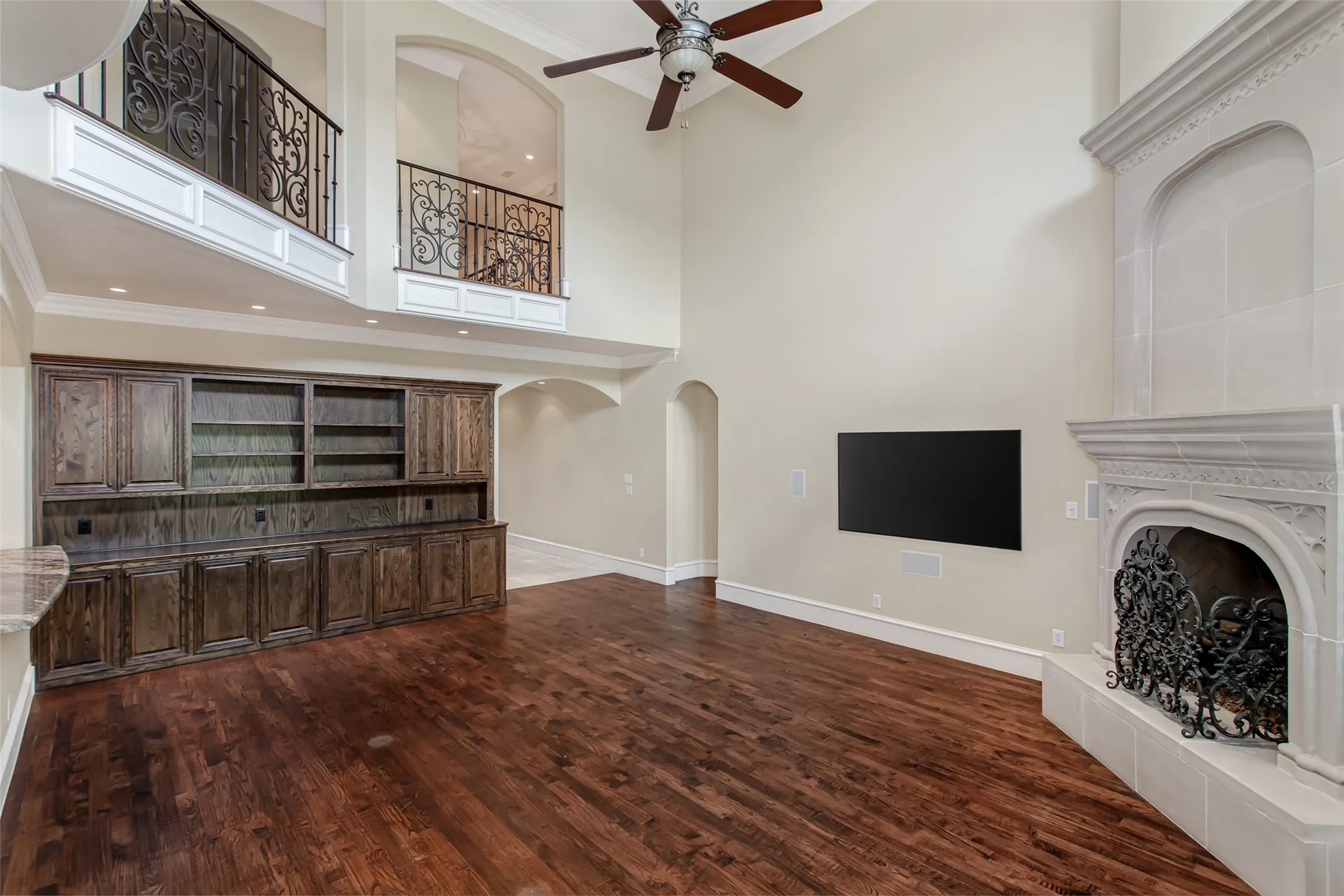 Breathtaking two-story living room featuring soaring ceilings, dramatic cast stone fireplace, custom built-in entertainment center, rich hardwood floors, and expansive wall space ideal for art or media.