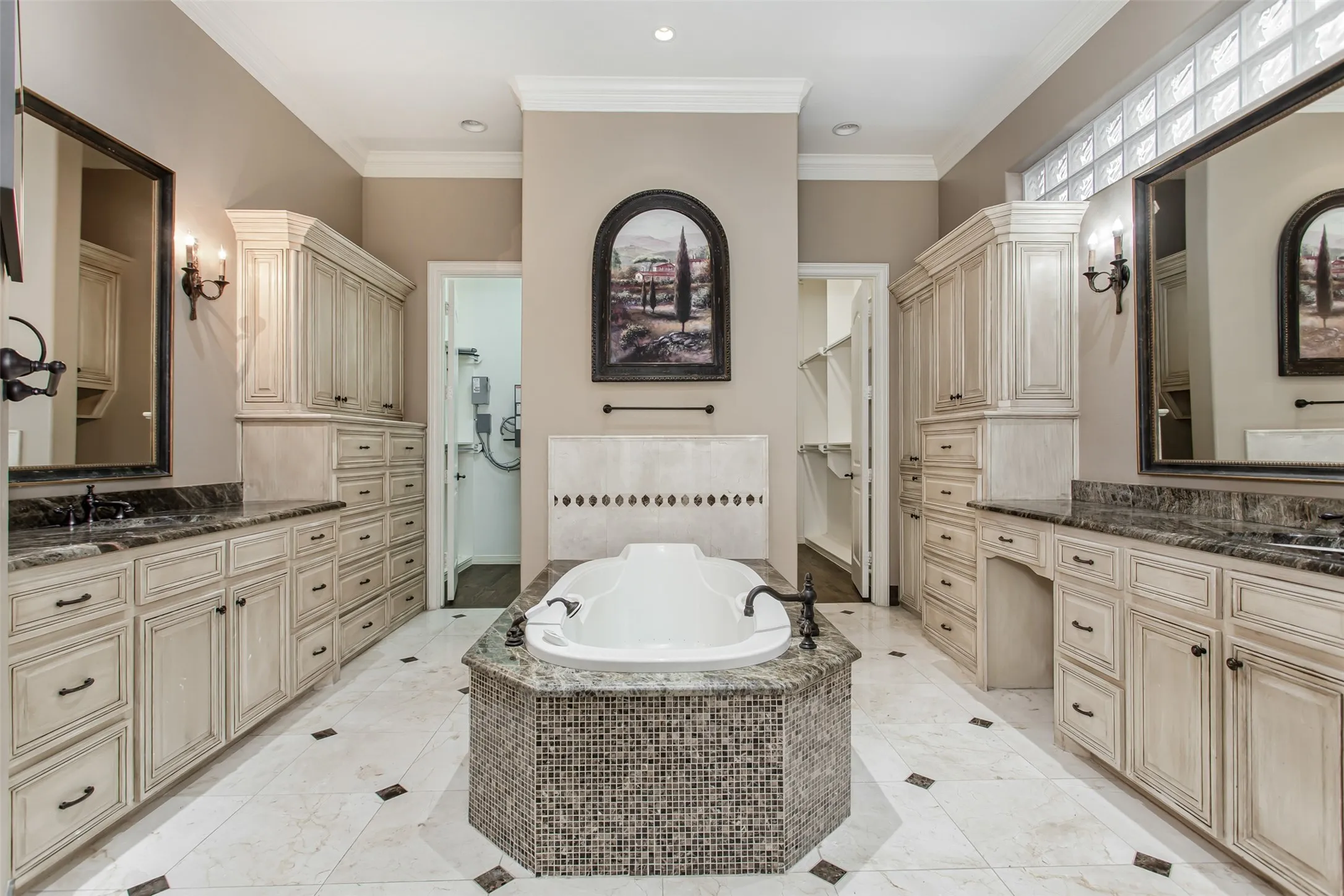 Resort-style primary bathroom featuring dual custom vanities, abundant built-in cabinetry, separate walk-in closets, a jetted soaking tub, and elegant marble flooring designed for everyday luxury.