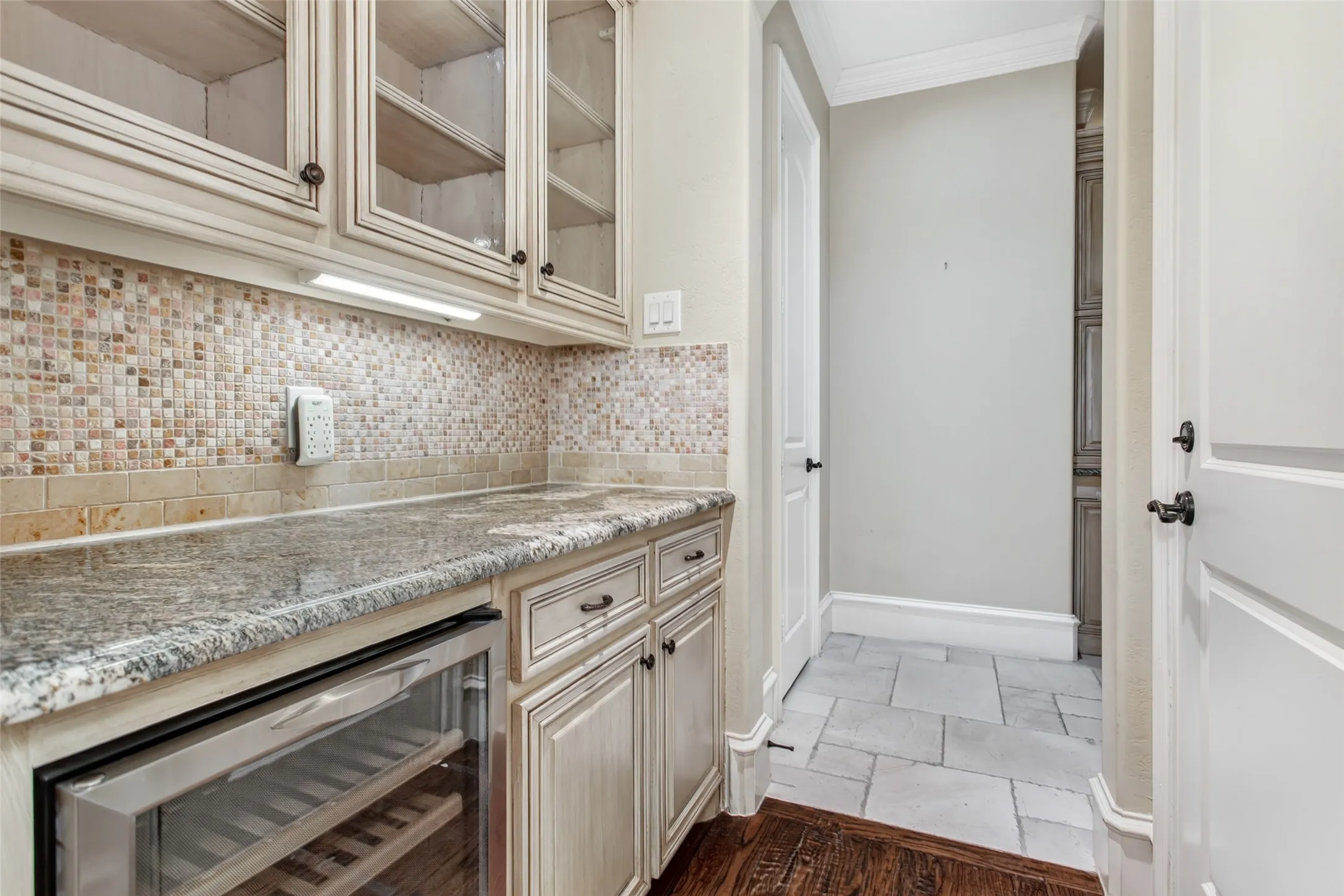 Well-appointed butler's pantry features granite countertops, custom cabinetry with glass display doors, beverage refrigerator, and abundant serving and storage space.