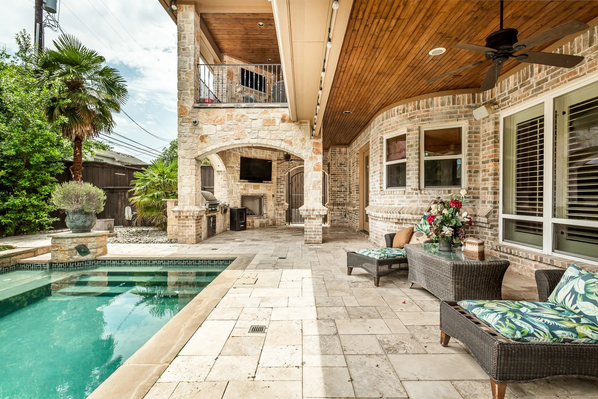 Multiple covered living areas provide comfortable spaces to relax or entertain, including a fully equipped outdoor kitchen with built-in grill, stone fireplace, and mounted television beneath a richly finished wood-plank ceiling. The second-story covered balcony overlooks the backyard and offers an additional outdoor gathering space with its own fireplace and television.