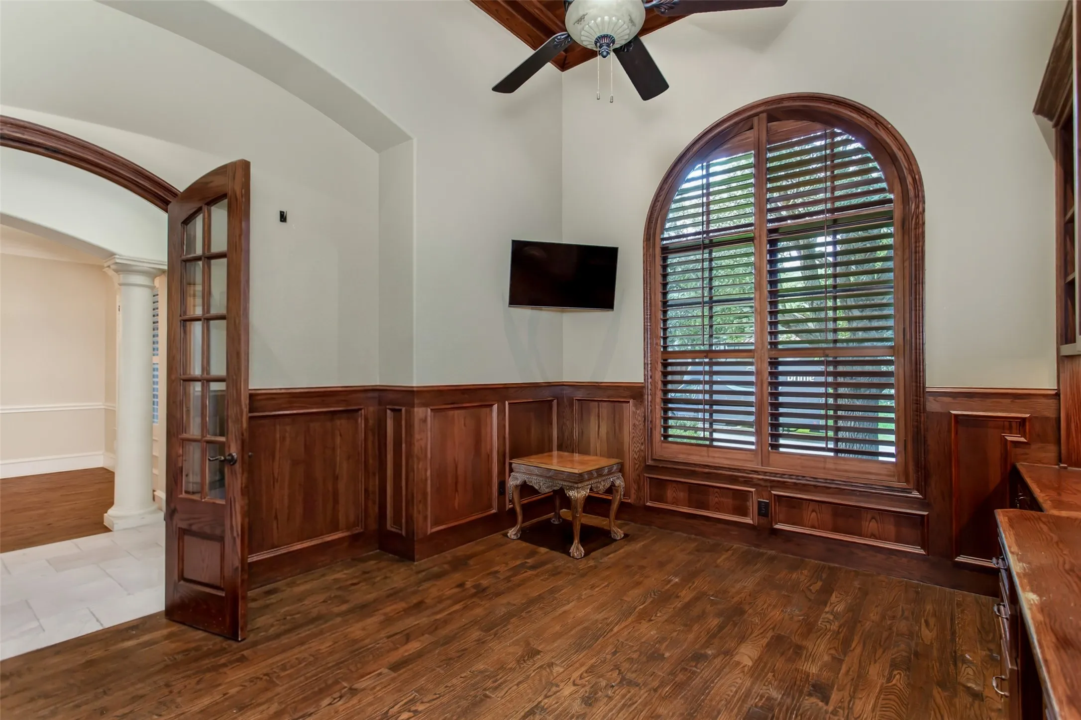 Distinguished executive office featuring rich custom wood paneling, hardwood floors, soaring ceilings, and a dramatic arched window overlooking the front grounds.