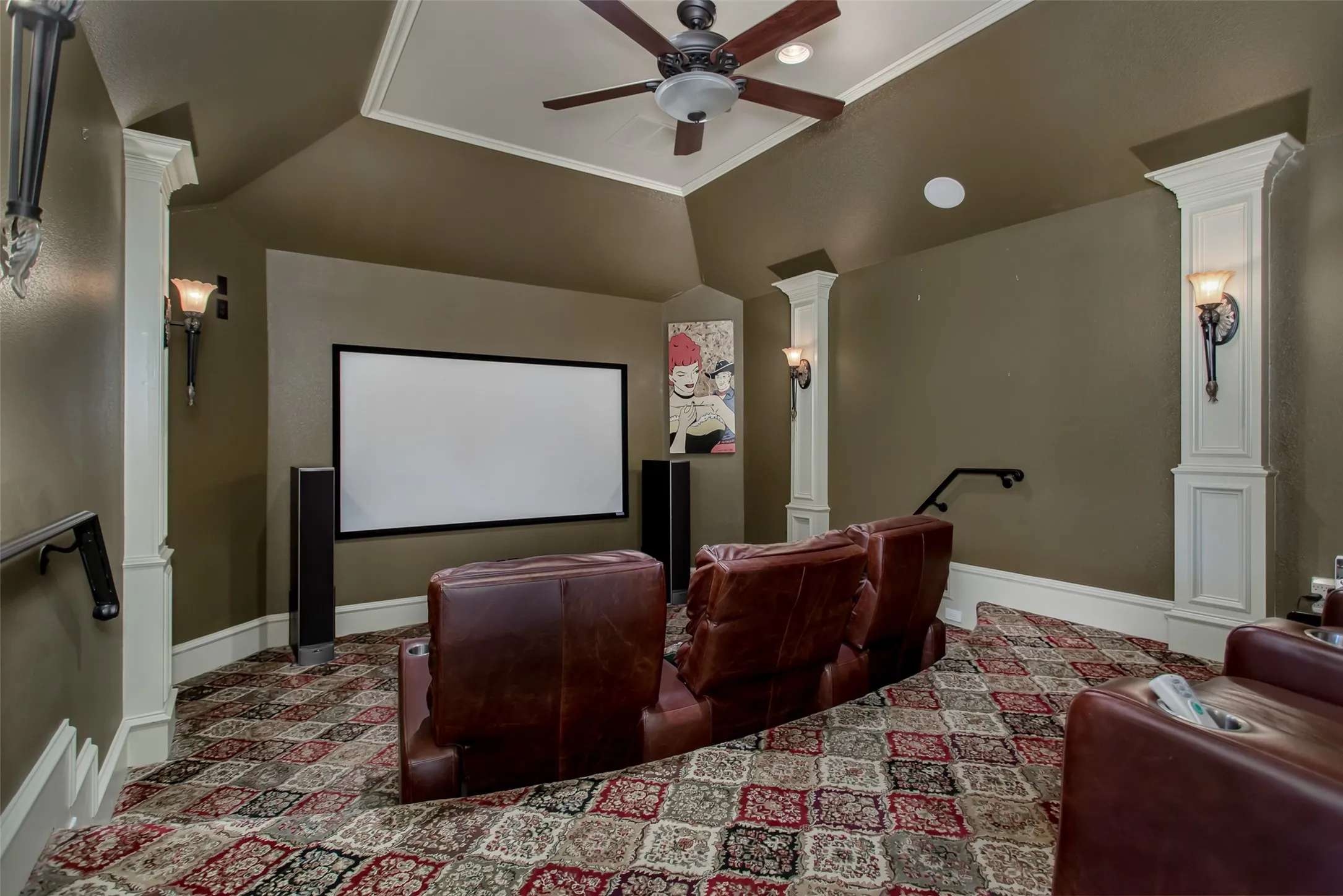 Dedicated tiered media room designed for the ultimate home theater experience, featuring stadium-style seating, projector screen, built-in surround sound, custom sconces, crown molding, and raised rear viewing platform—perfect for movie nights, sporting events, or gaming.