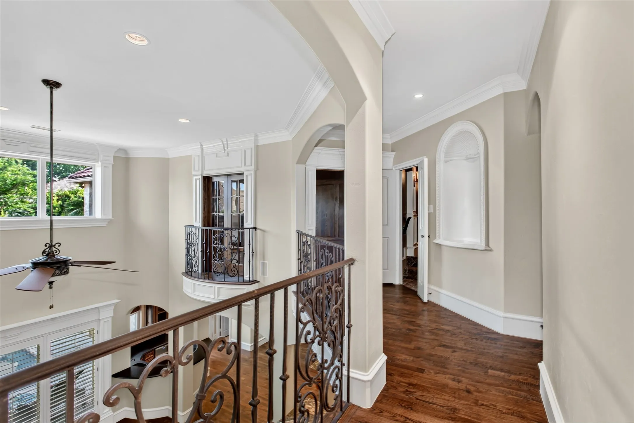 The upstairs gallery overlooks the dramatic two-story living area below, showcasing rich hardwood flooring, custom wrought-iron railings, elegant architectural details, and abundant natural light. This thoughtfully designed landing creates a beautiful transition between the home's secondary bedrooms while adding to the open, airy feel of the floor plan.
