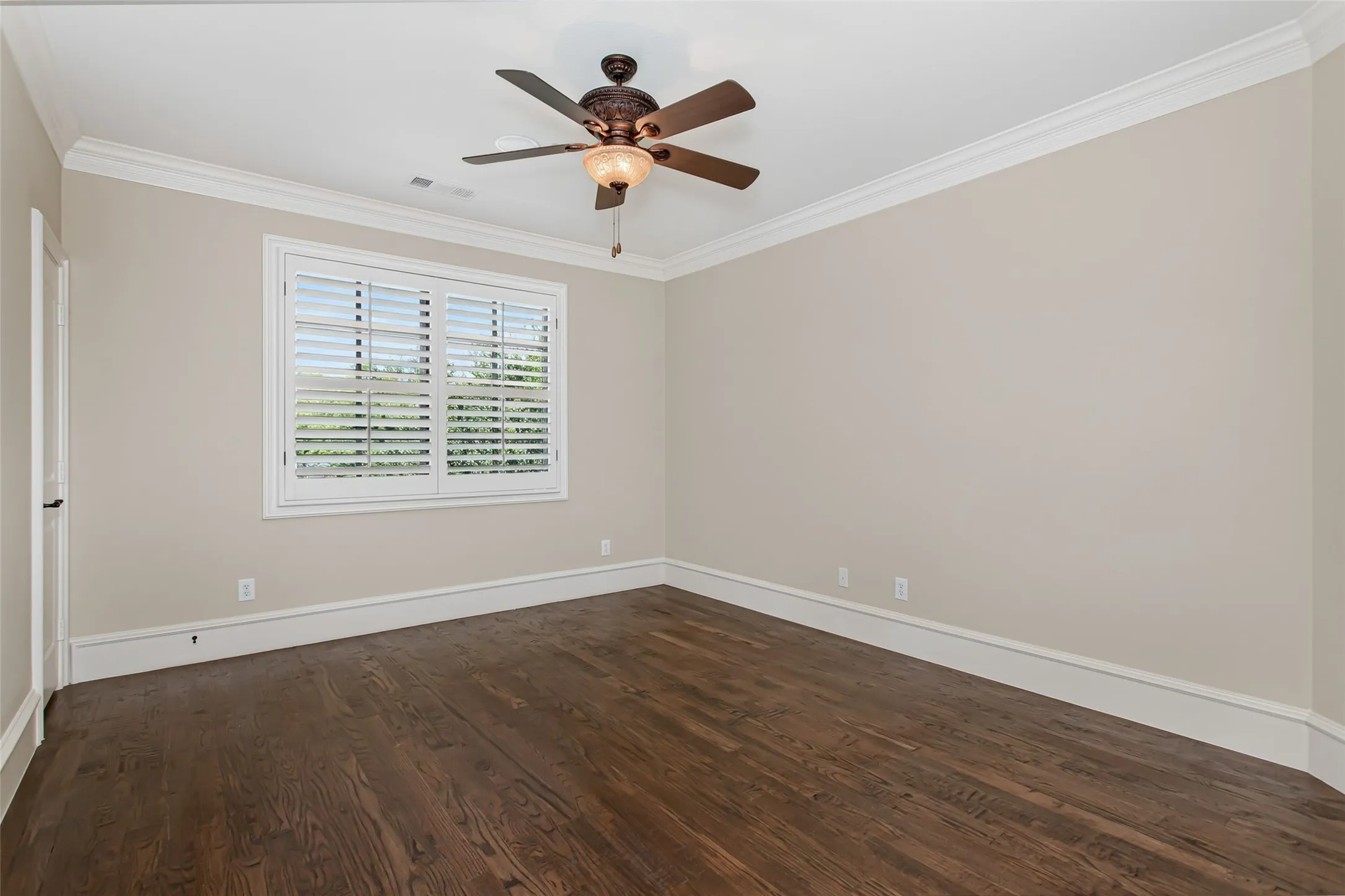This spacious secondary bedroom offers rich hardwood floors, crown molding, plantation shutters, and a tray ceiling.