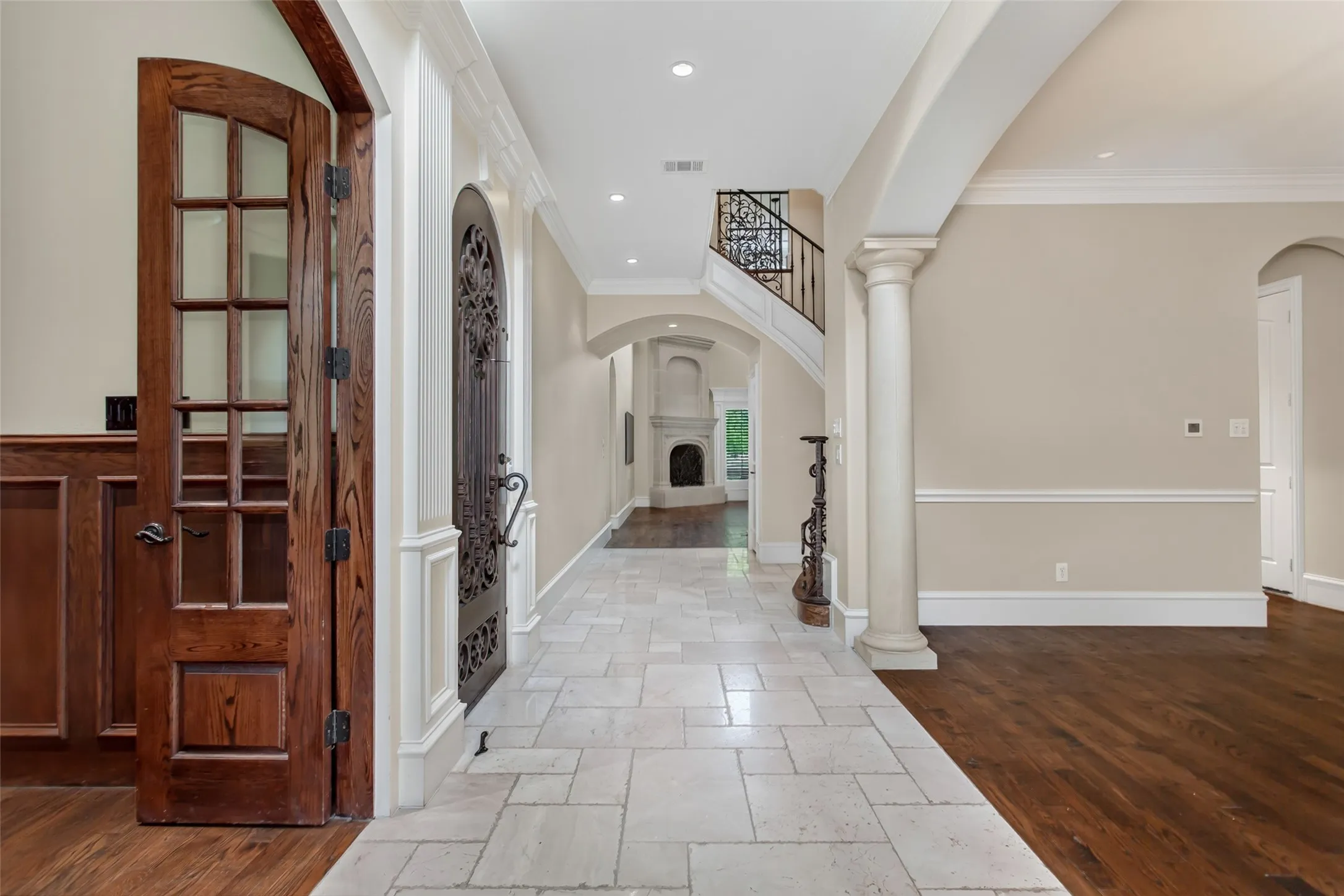 The grand foyer welcomes guests with terrazzo tile, a custom iron entry door, elegant millwork, and sightlines to the living spaces beyond.