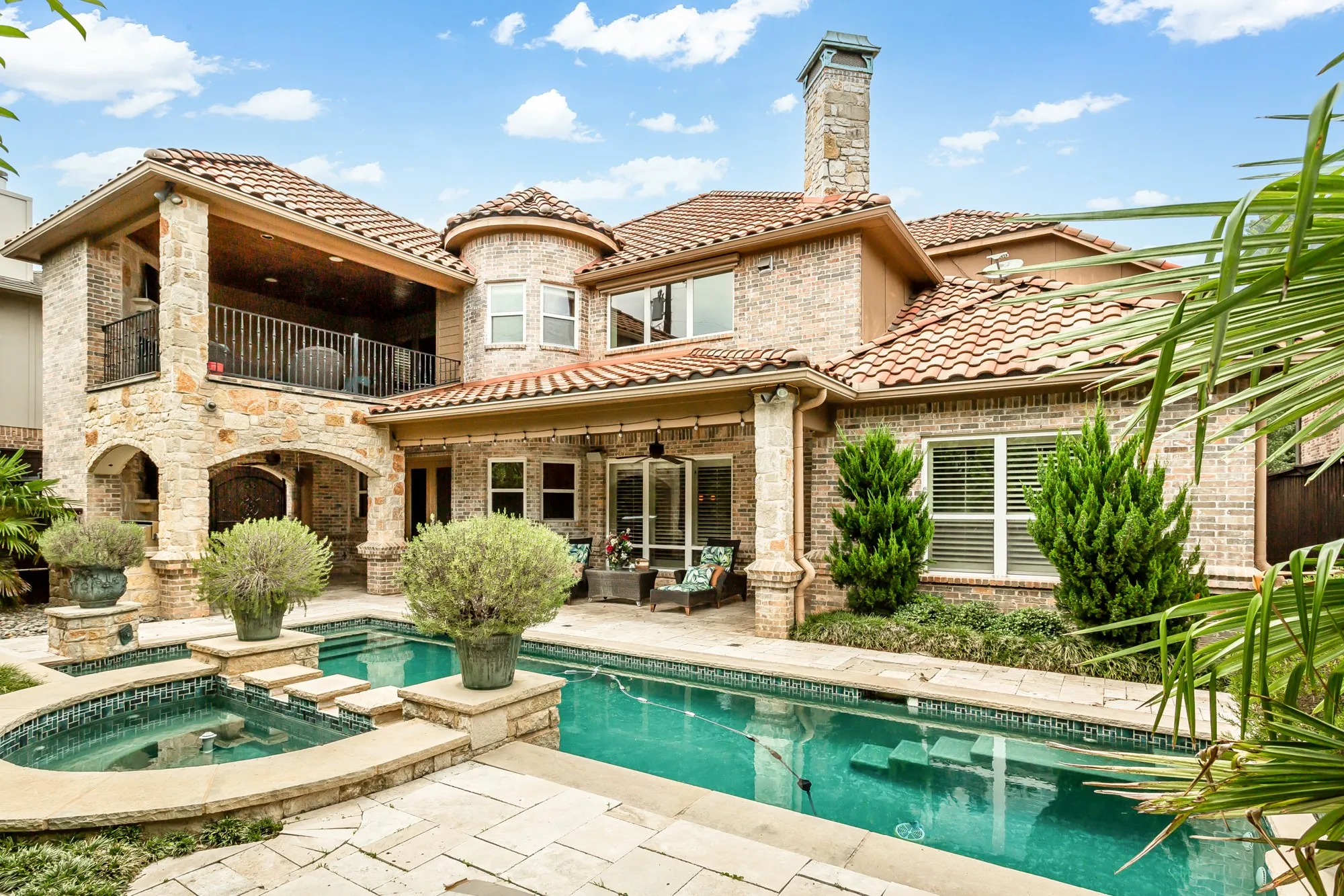 The backyard is designed for luxury outdoor living, anchored by a stunning custom pool and raised spa with cascading water features, tanning ledge, and elegant travertine decking.