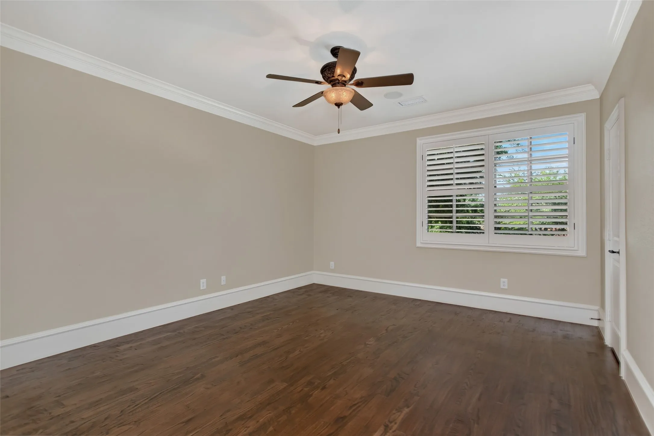 Spacious upstairs bedroom with hardwood floors, crown molding, plantation shutters, ceiling fan, and a private ensuite bath.