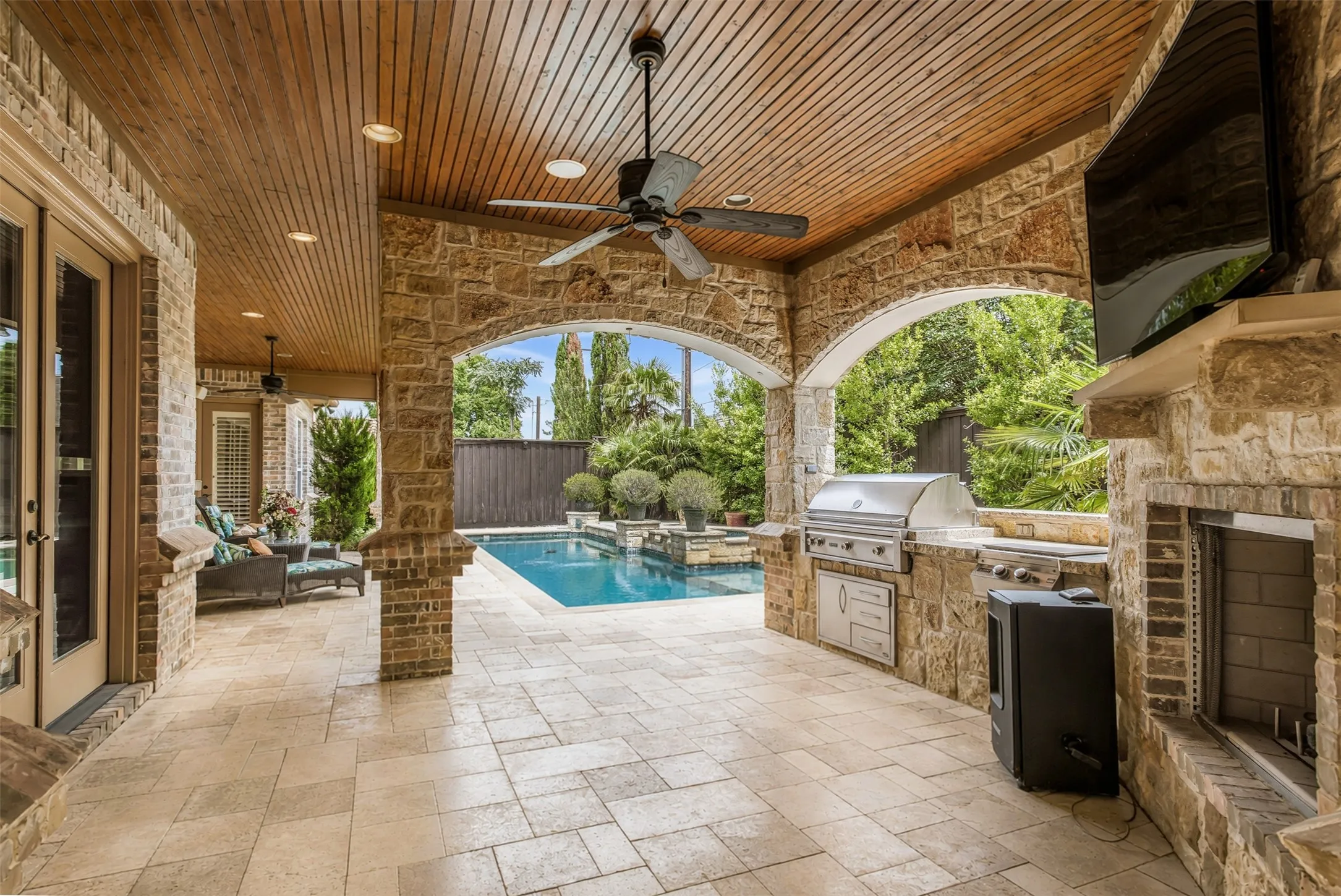 The fully equipped outdoor kitchen features a built-in stainless steel grill, side burner, sink, and generous prep space, making it ideal for hosting family and friends. Travertine flooring, elegant stone columns, and seamless access to the resort-style pool and spa complete this exceptional backyard retreat.