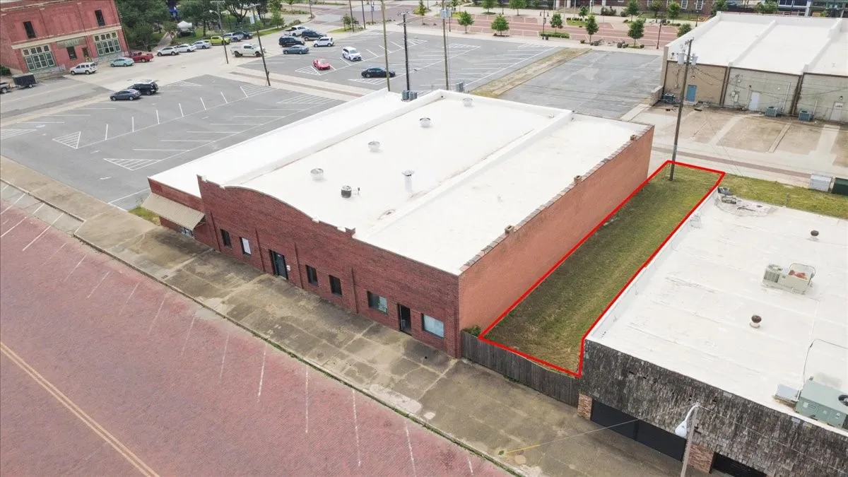 Brick commercial building with a flat roof and a fenced grass lot