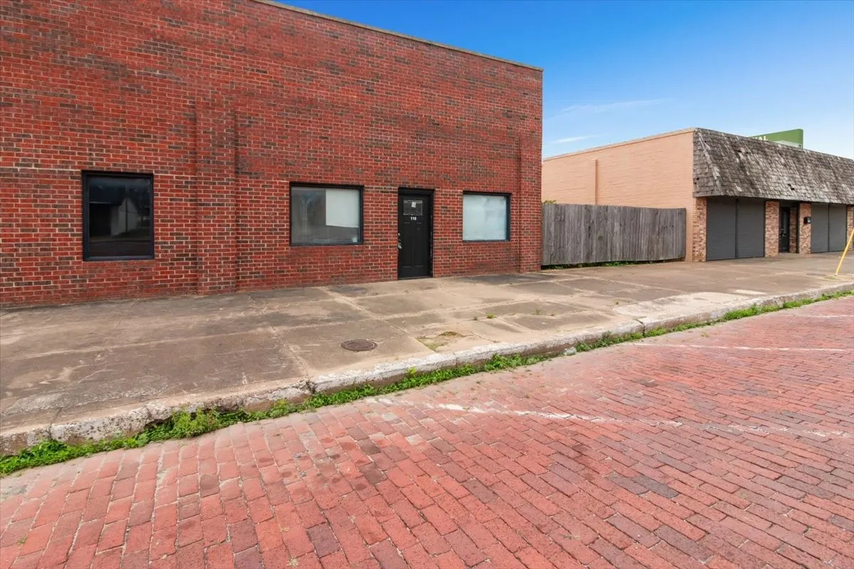 Brick exterior building with multiple window openings and a dark entry door