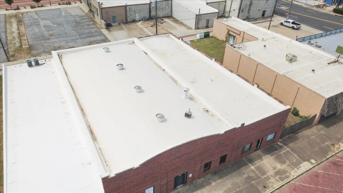 Commercial building featuring a brick facade with multiple windows, two flat white roofs, and several rooftop ventilation units