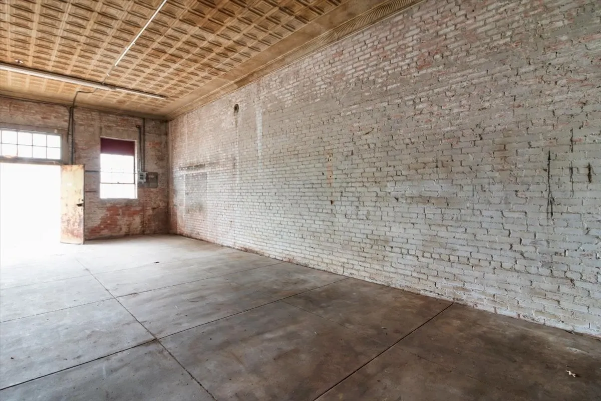 Spacious interior featuring exposed brick walls, a textured ceiling, concrete flooring, and multiple window openings