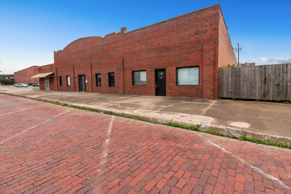 Brick facade commercial building featuring an arched parapet, multiple black entry doors, and large windows