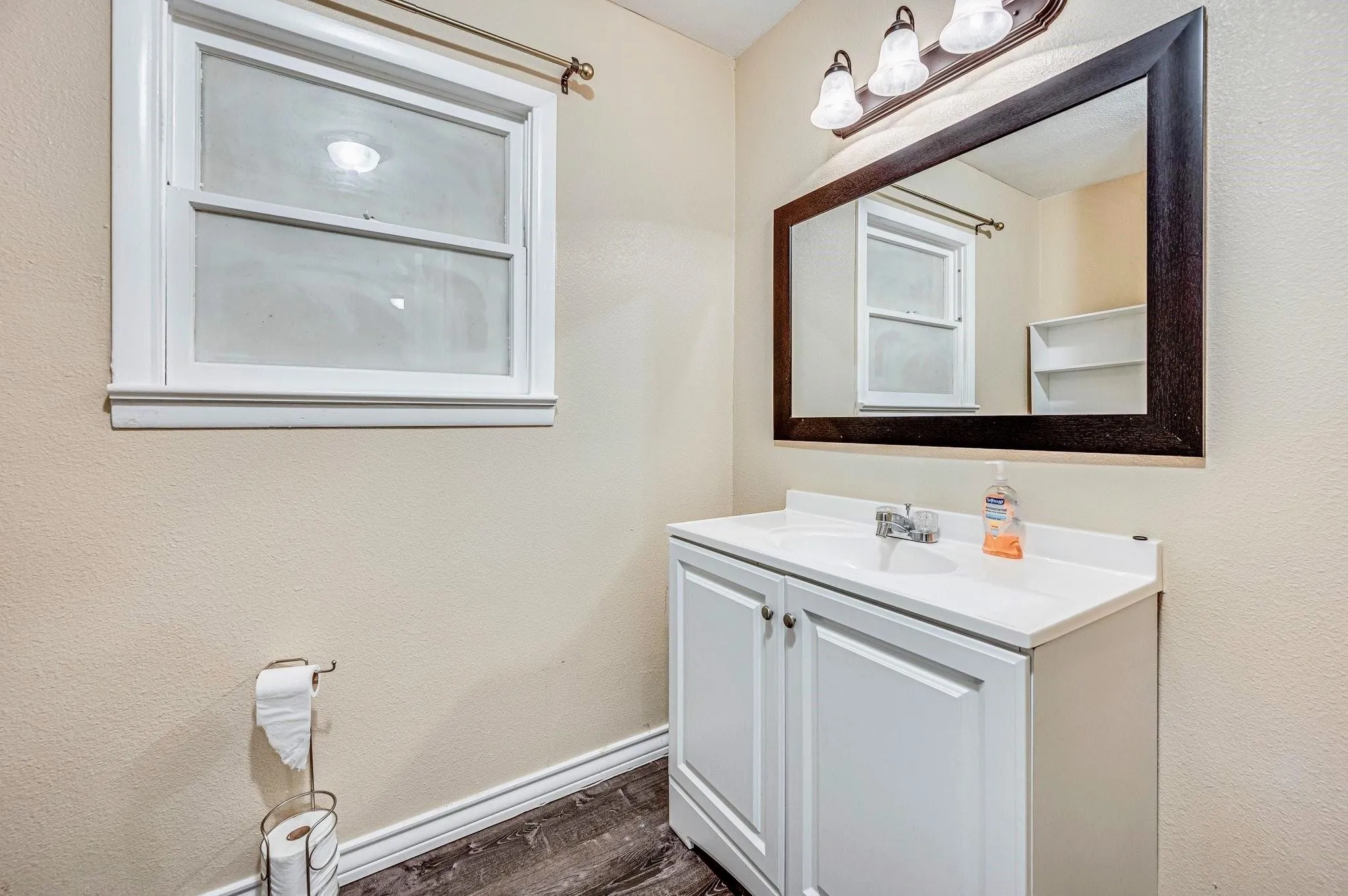 Bathroom vanity with a white countertop and base cabinet, featuring a large framed mirror and a three-light fixture